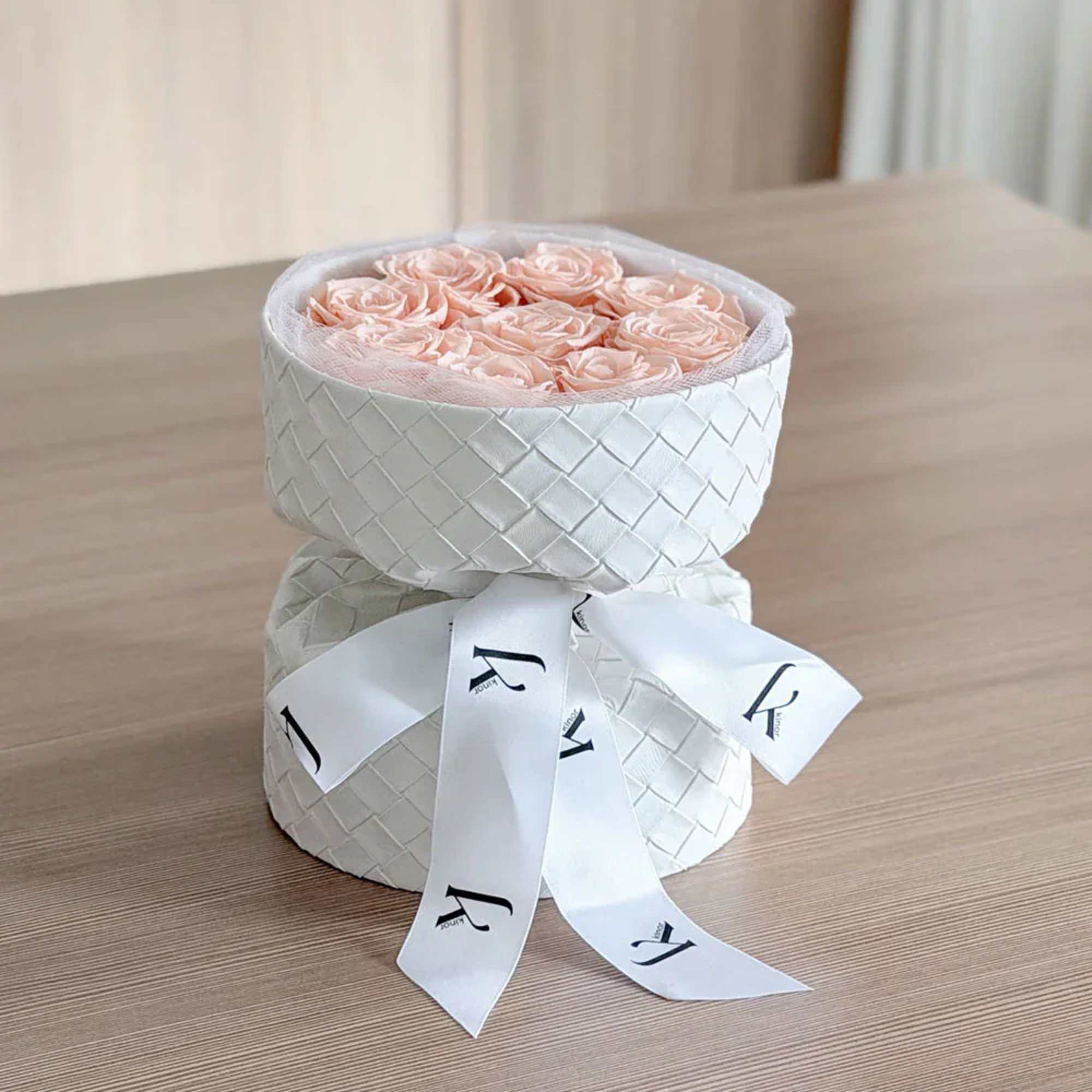 Round box of pale pink roses tied with a white ribbon