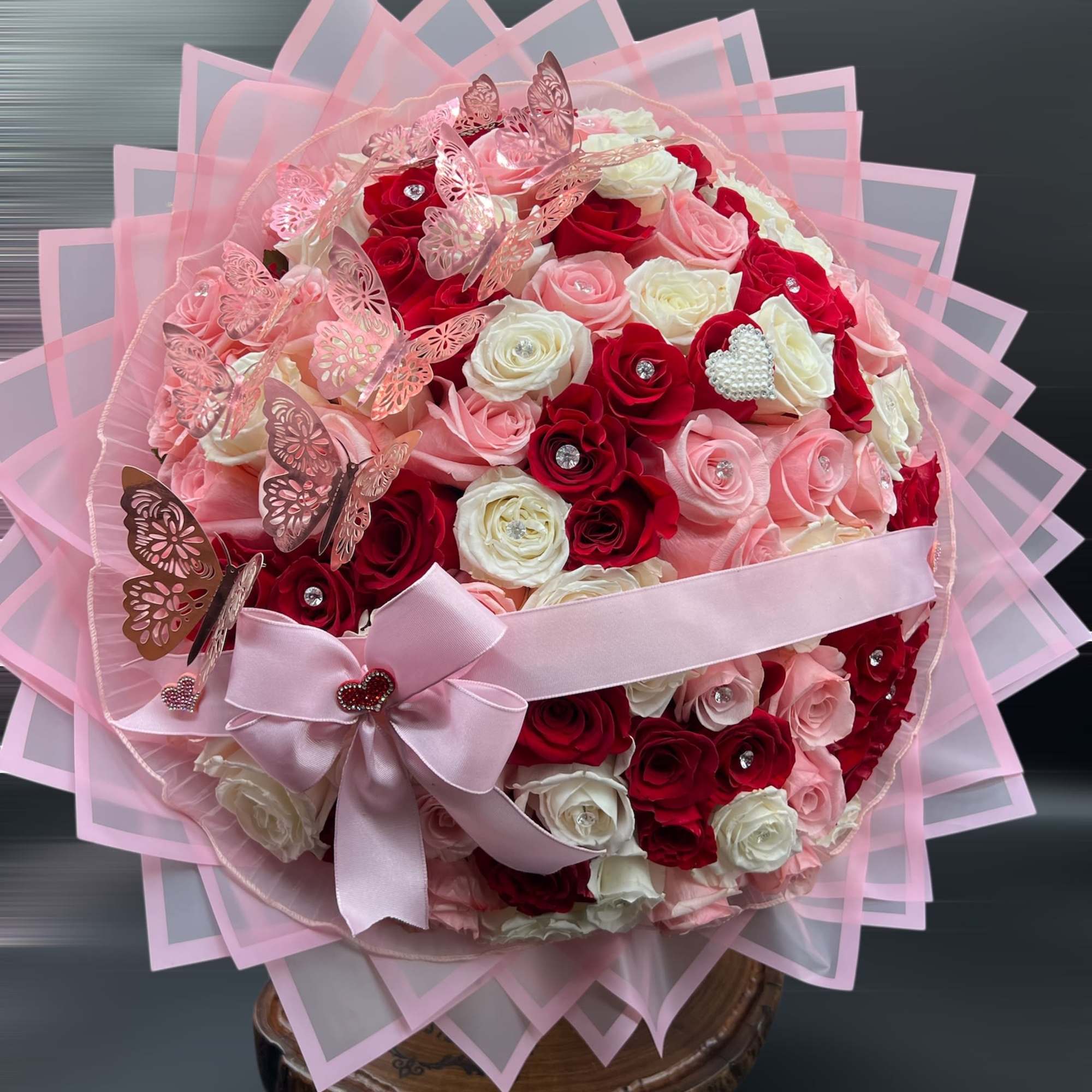 Round bouquet of pink, red, and white roses with a pink ribbon and butterfly decorations