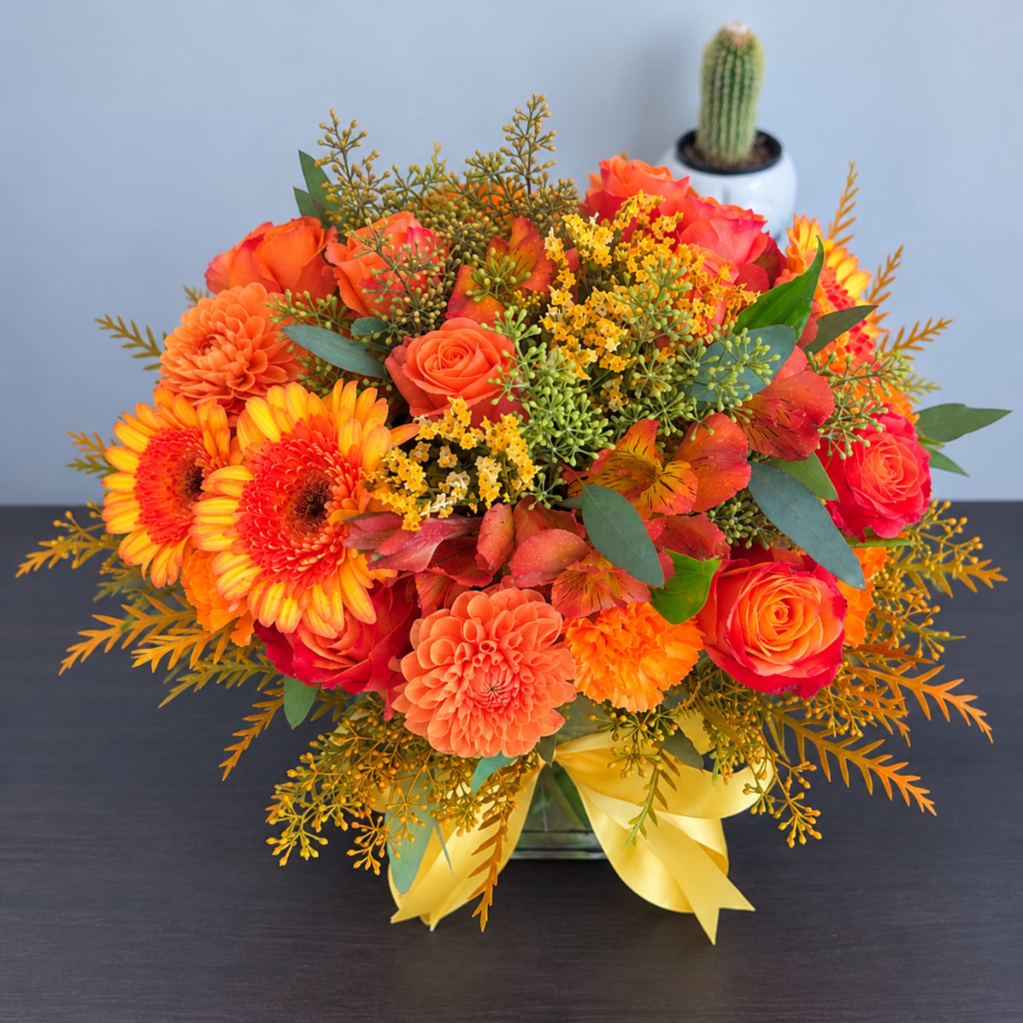 Orange and pink mixed bouquet in a glass vase with a yellow ribbon