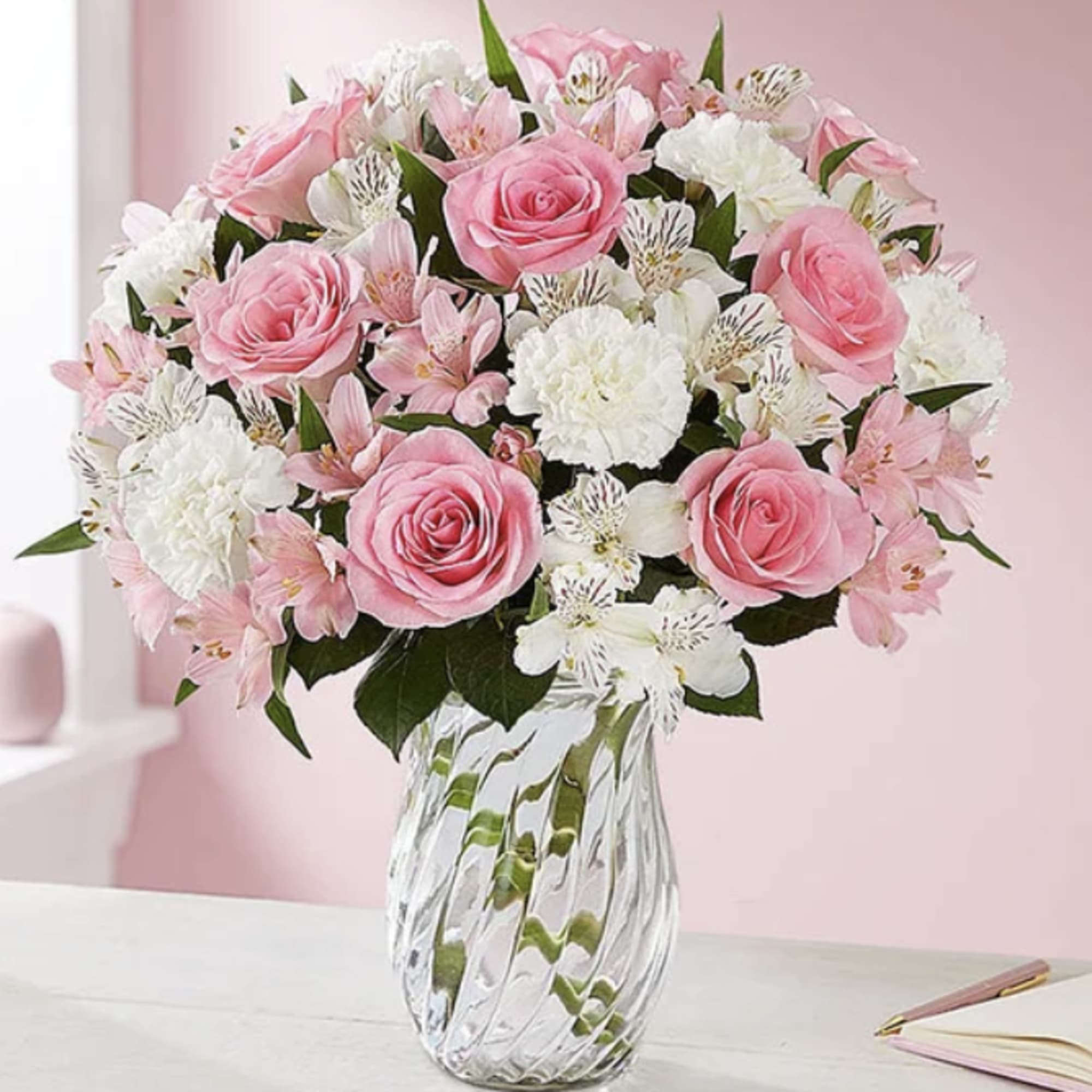 Pink roses, white carnations, and alstroemeria arranged in a clear glass vase