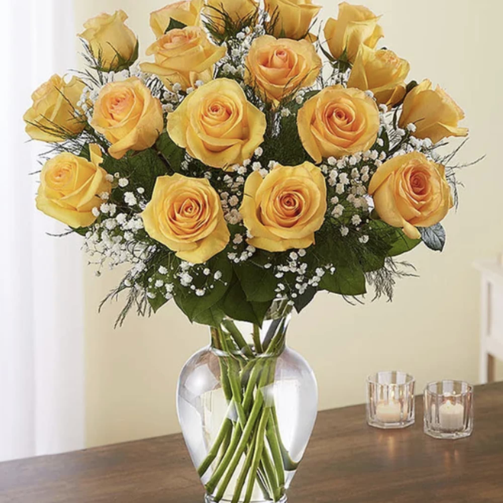Bouquet of yellow roses with white filler flowers in a clear glass vase on a wooden table