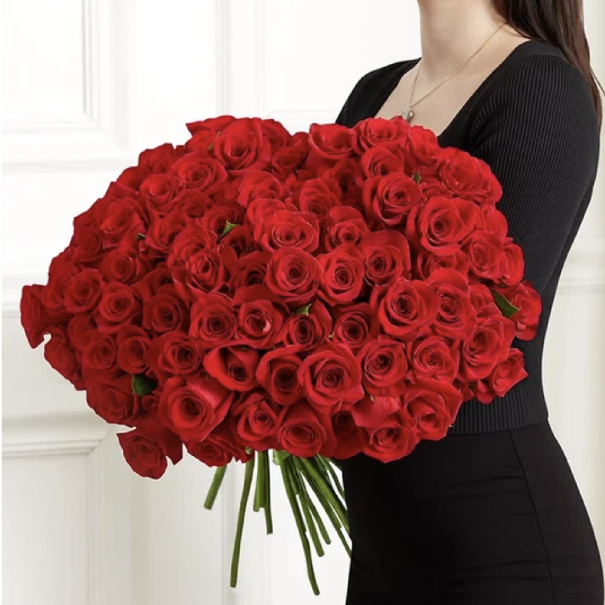 Large armful bouquet of long-stemmed red roses held by a person in black clothing