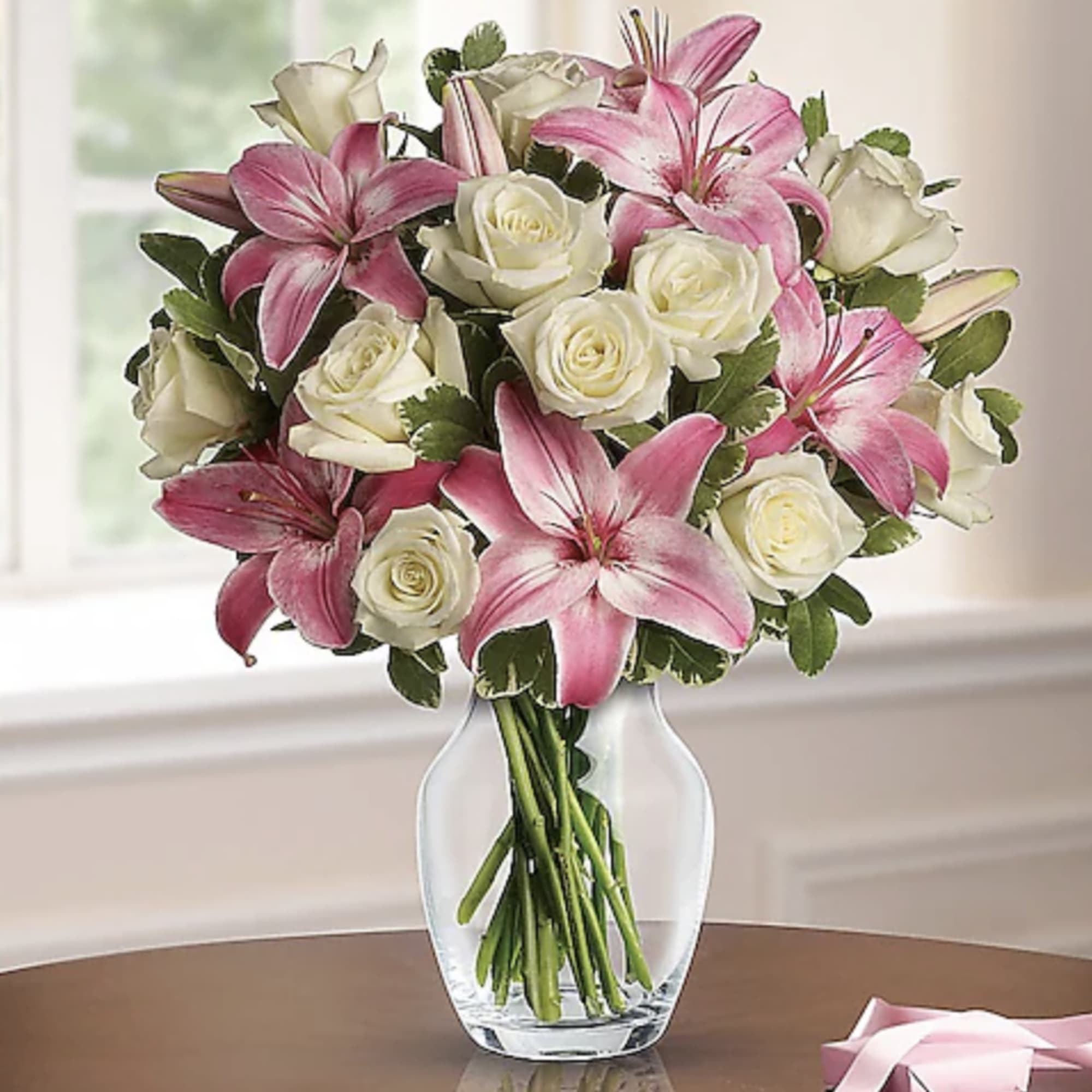 Pink lilies and white roses arranged in a clear glass vase on a table.