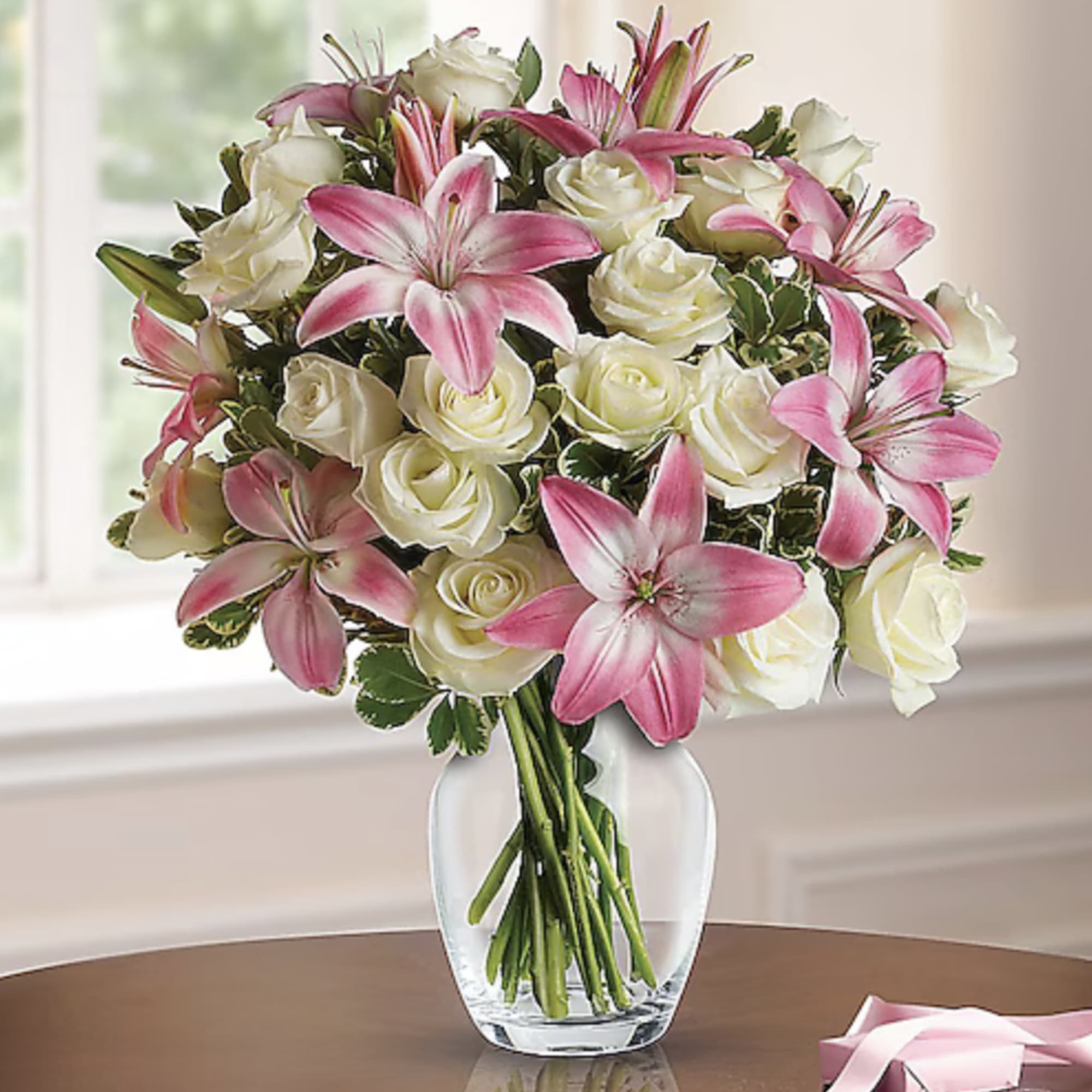 Arrangement of pink lilies and white roses in a clear glass vase on a table