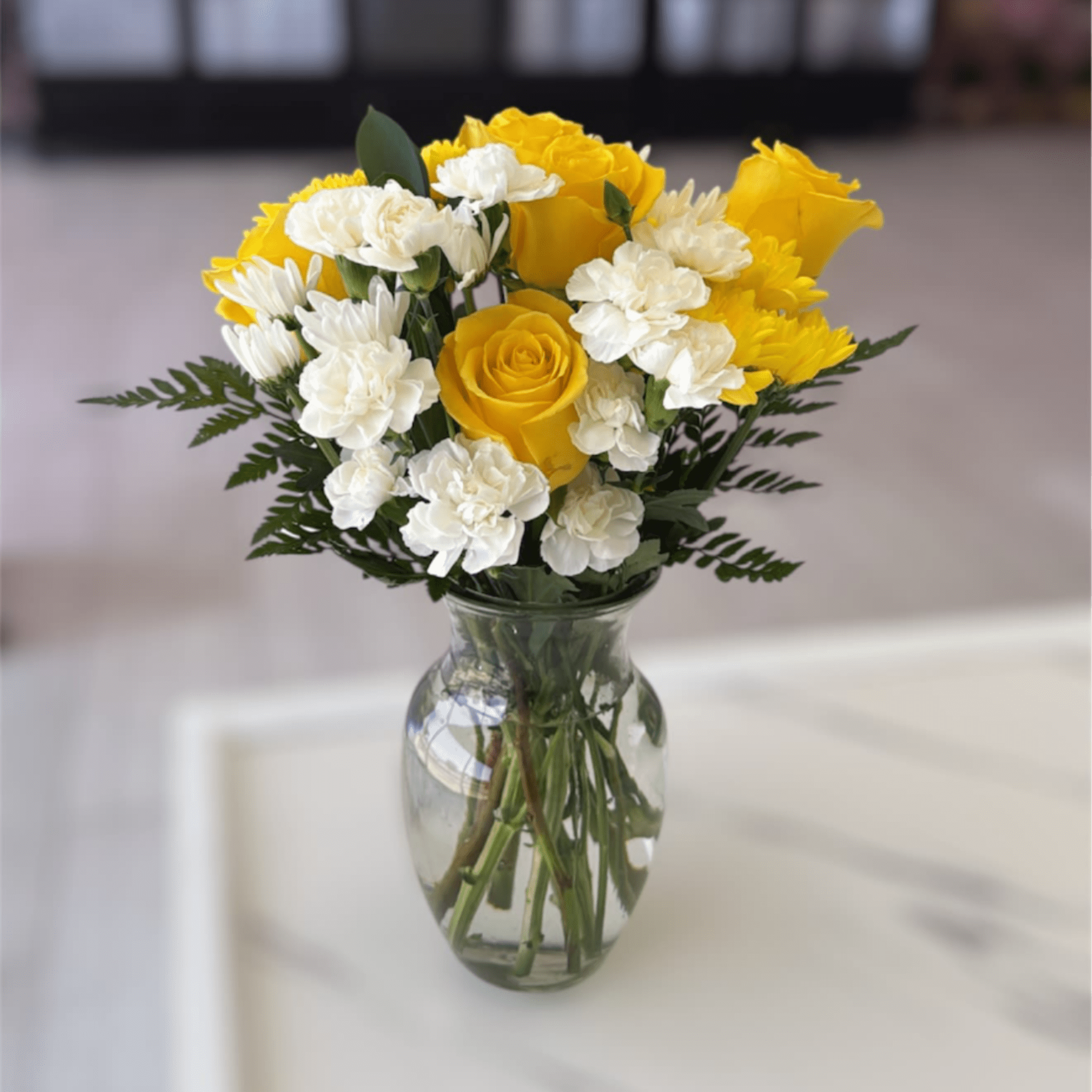 Yellow roses and white carnations in a clear glass vase