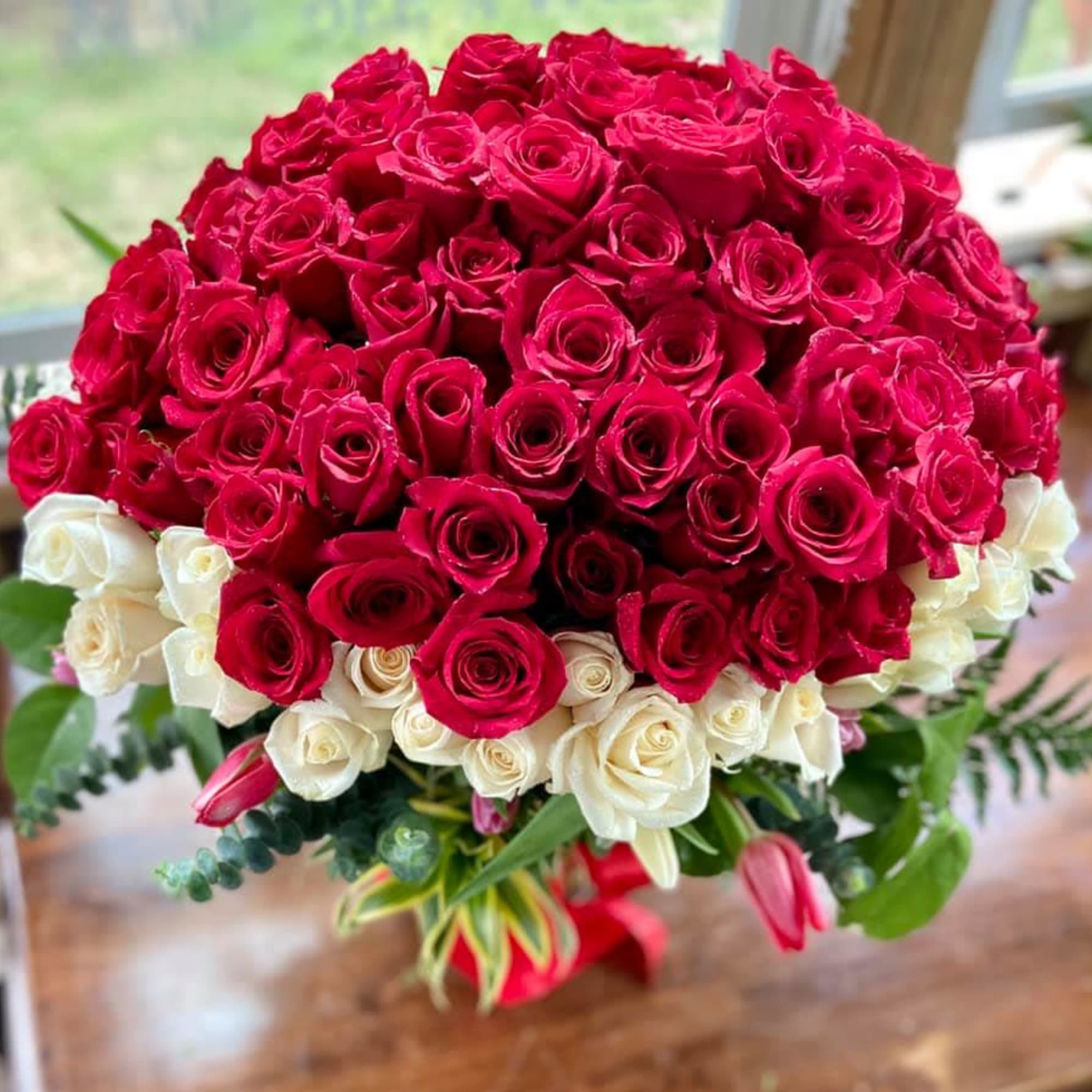 Large bouquet of red and white roses with a few pink tulips and foliage in a vase