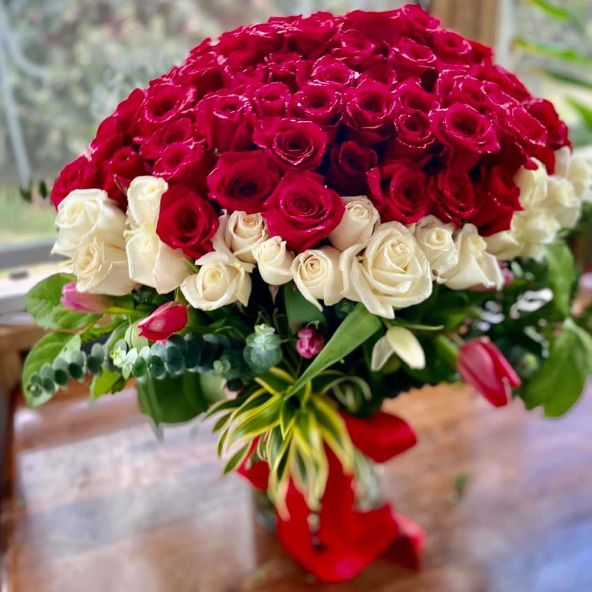 Large dome arrangement of red and white roses with pink tulips in a glass vase