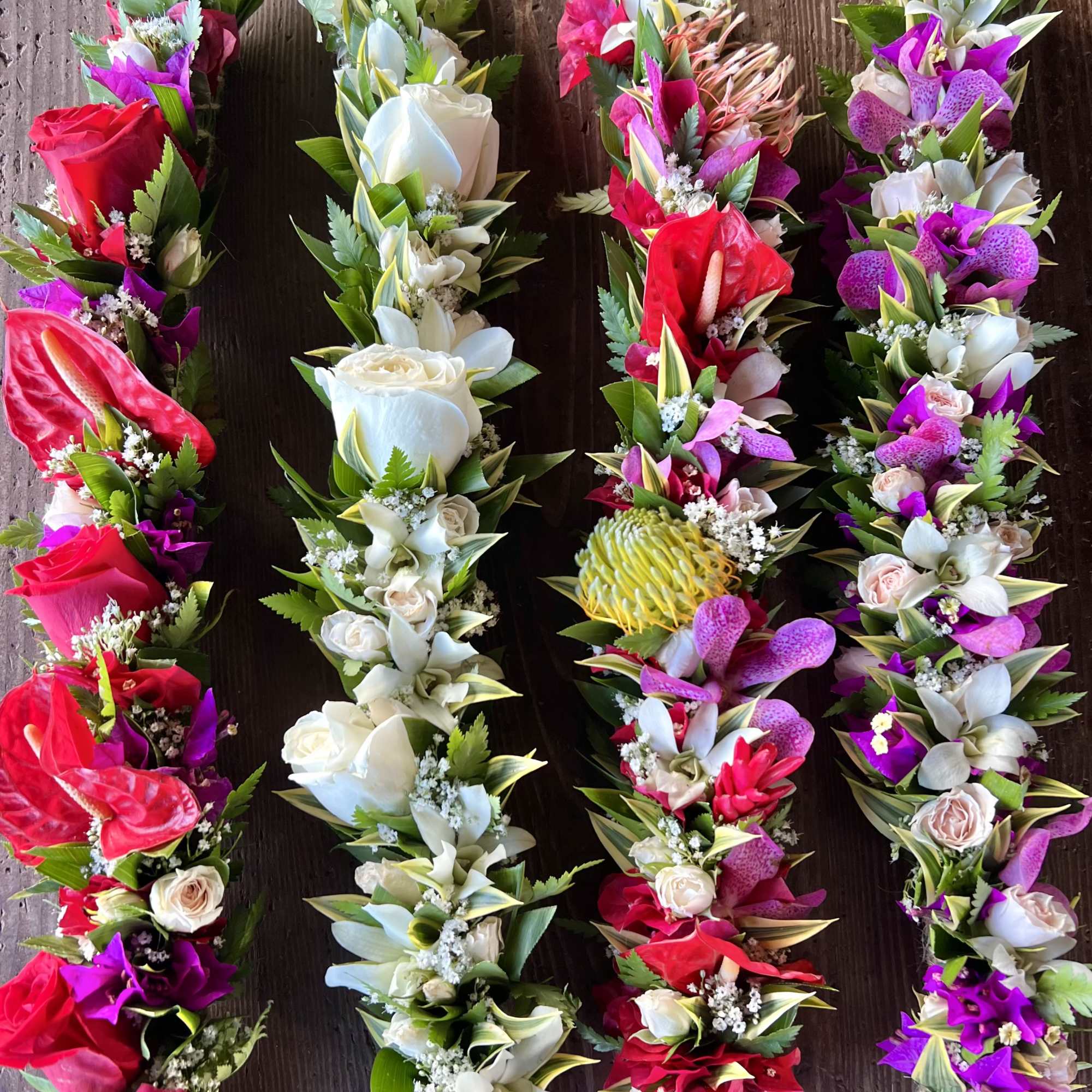 Set of four colorful floral garlands with red, white, pink, and purple blooms on a wooden surface