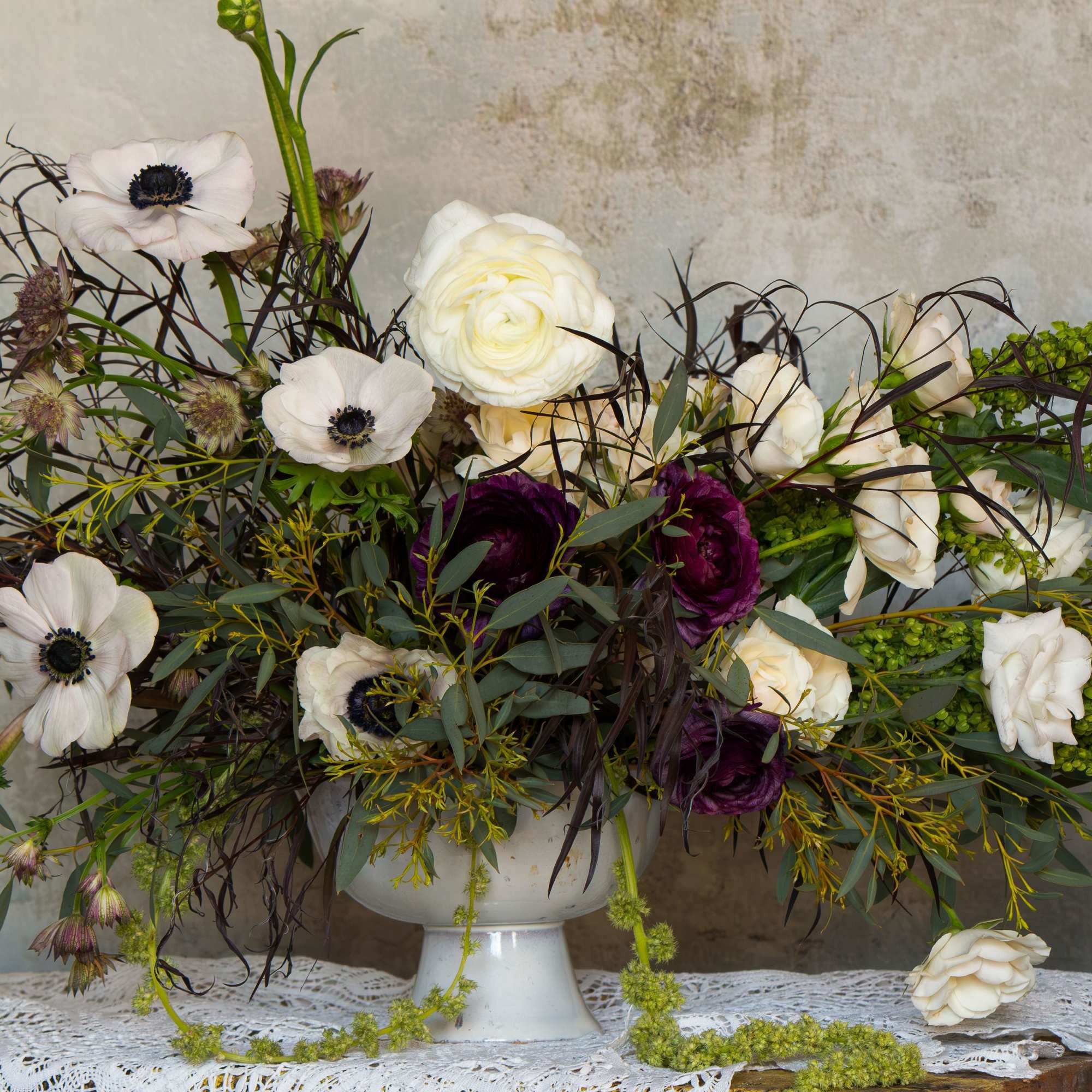 White and deep purple floral arrangement in a white pedestal vase