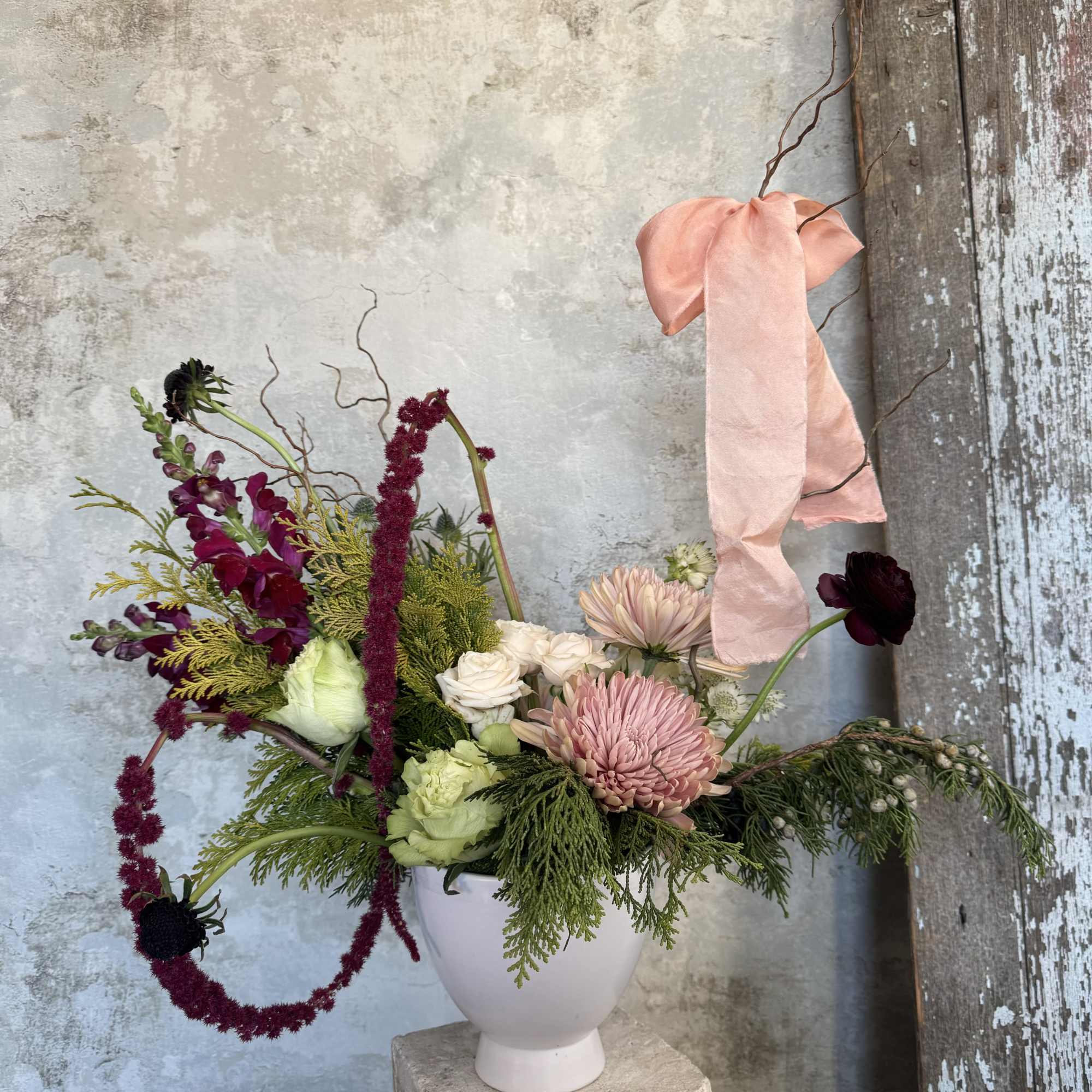 Mixed floral arrangement in a white vase with a pink ribbon
