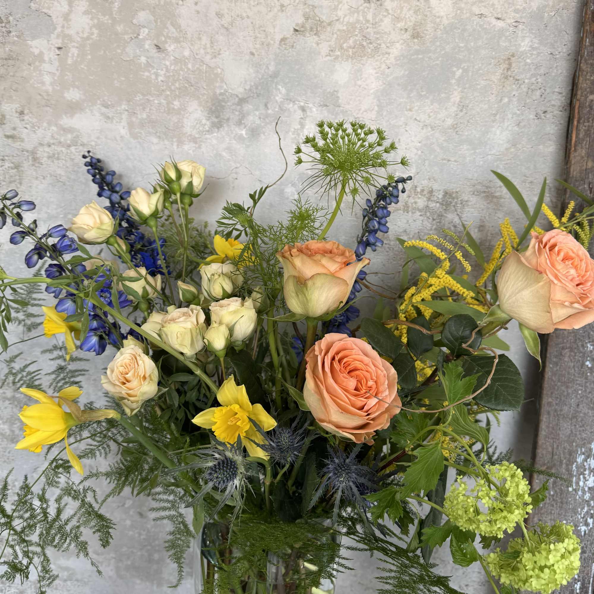 Mixed bouquet with peach roses, yellow daffodils, and blue flowers