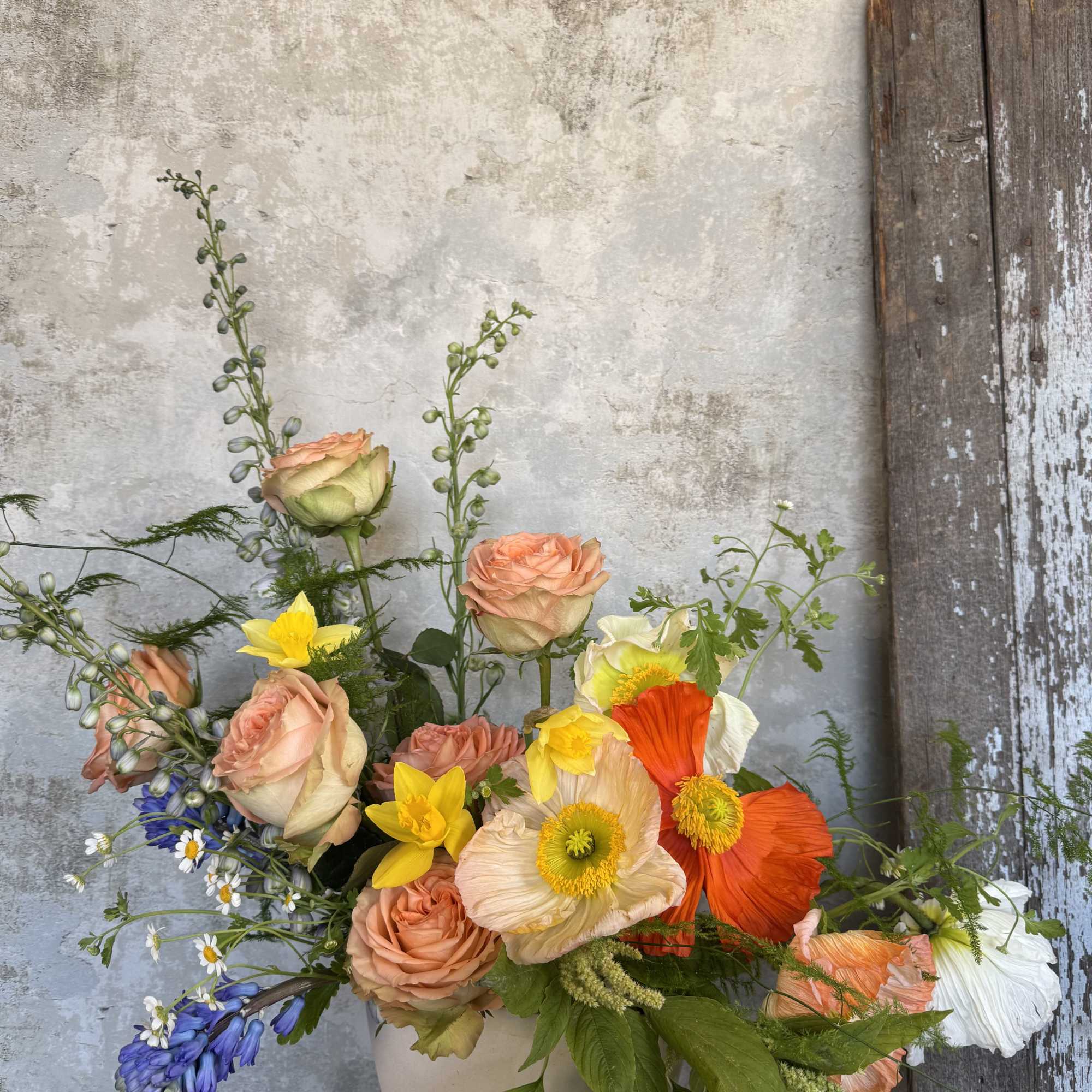 Mixed bouquet of peach roses, poppies, and yellow flowers in a white vase