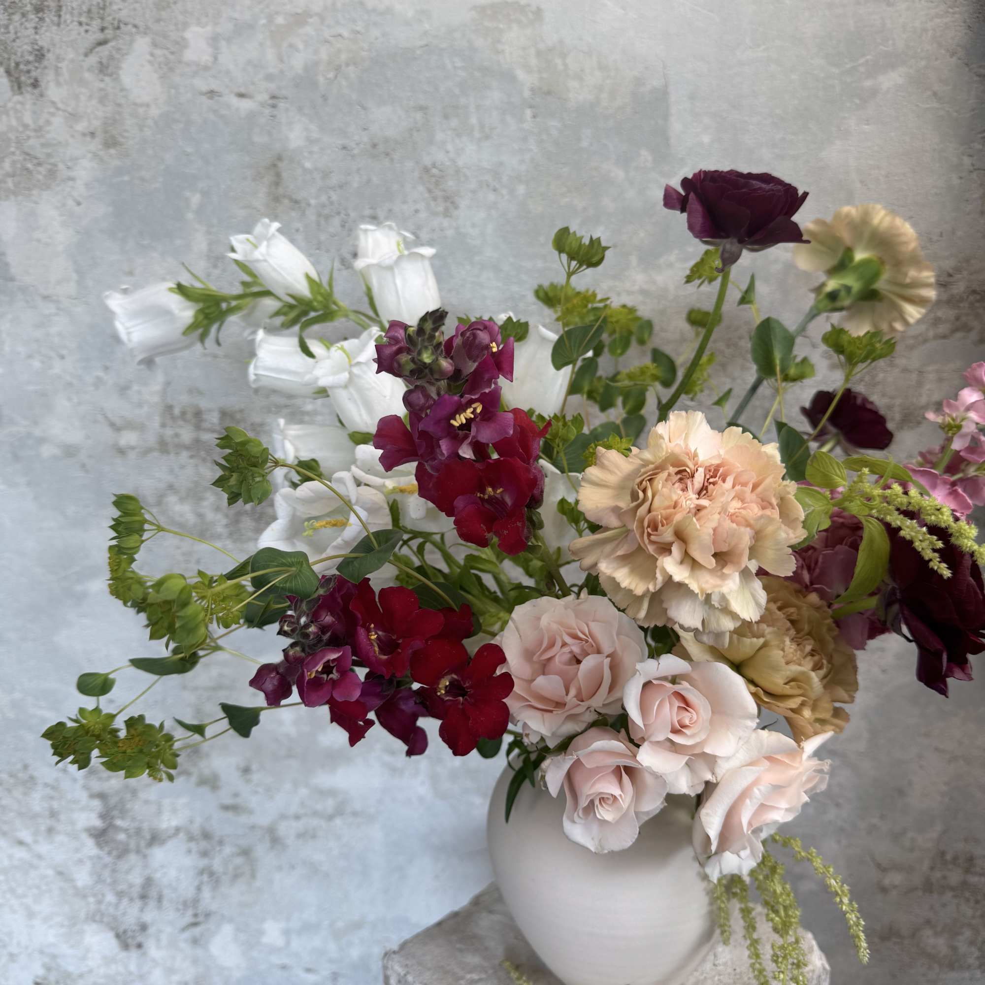Mixed bouquet of roses, carnations, and white bell-shaped flowers in a white vase
