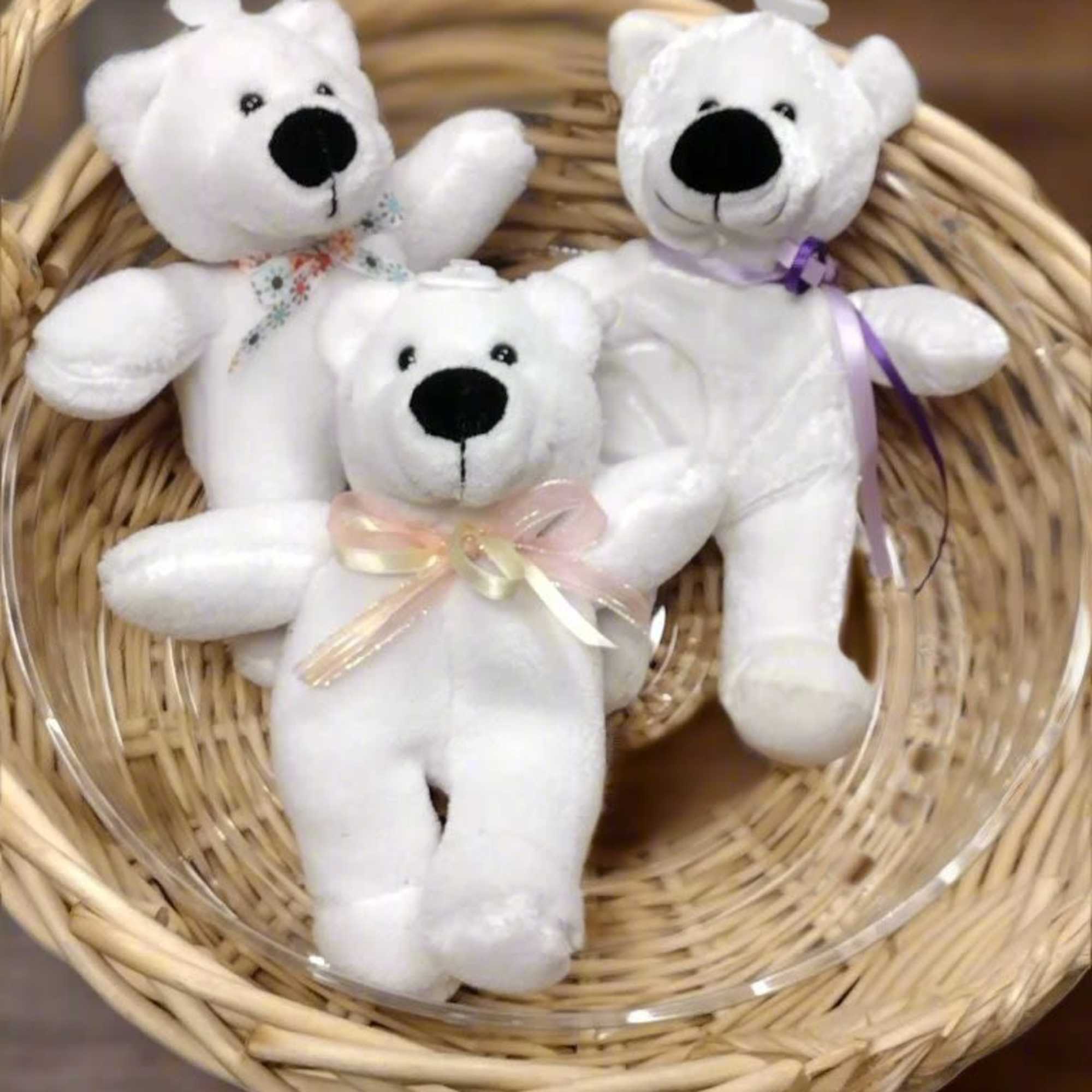 Three small white teddy bears with ribbons arranged in a wicker basket