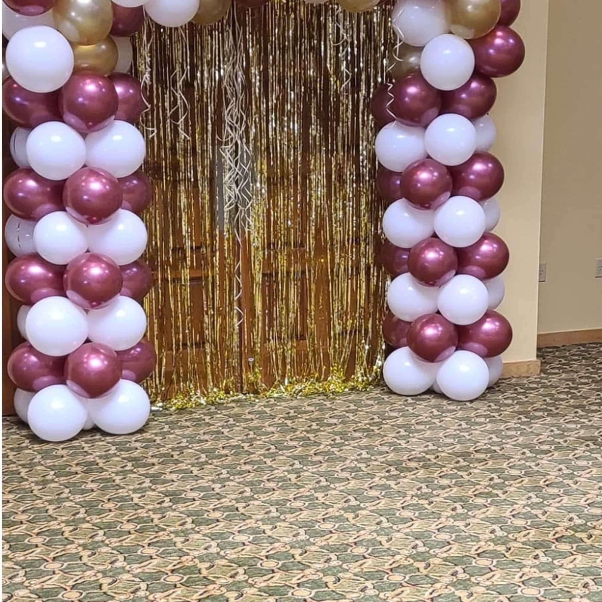 Balloon arch in burgundy, white, and gold with a metallic fringe backdrop