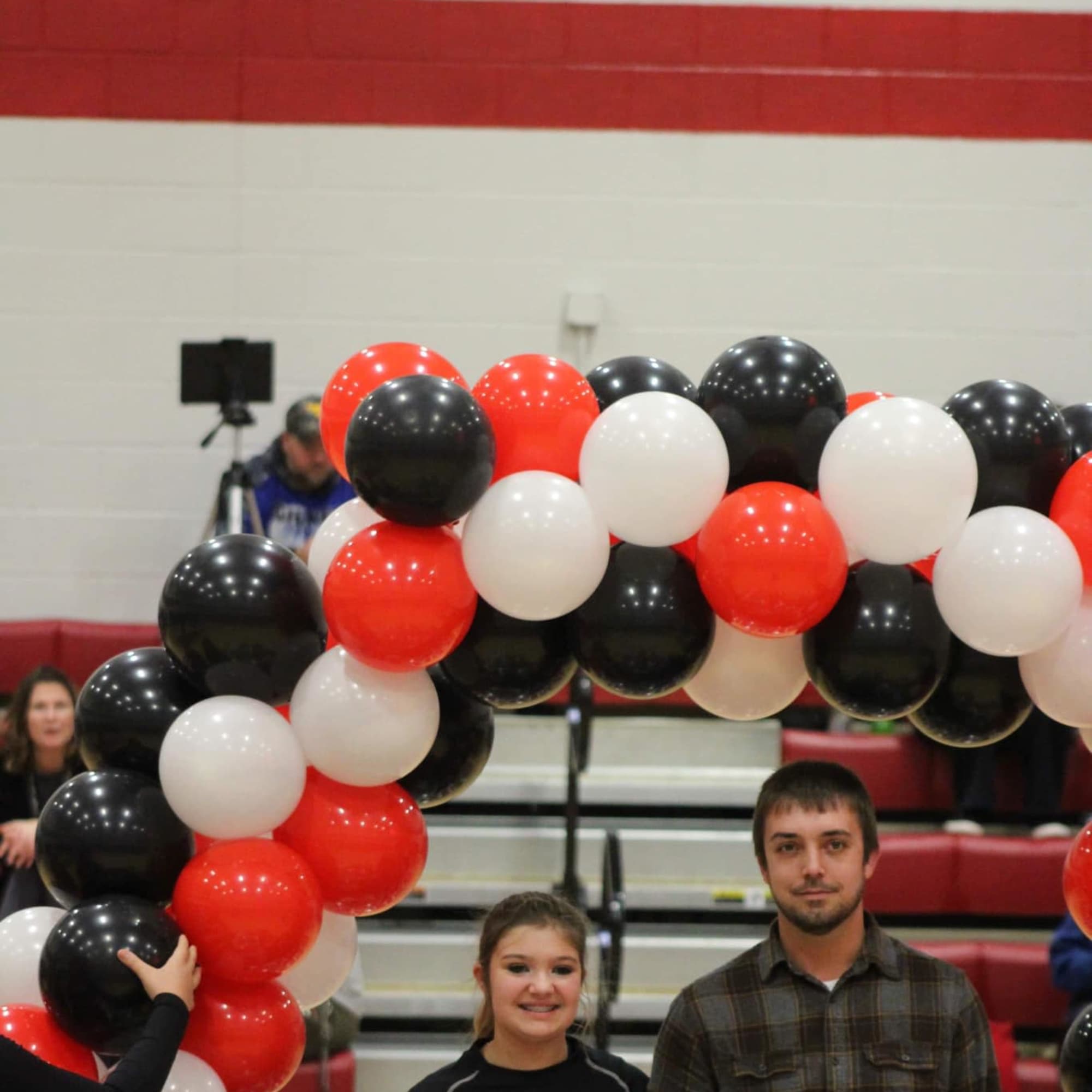 Red, white, and black balloon arch with a girl holding a small bouquet