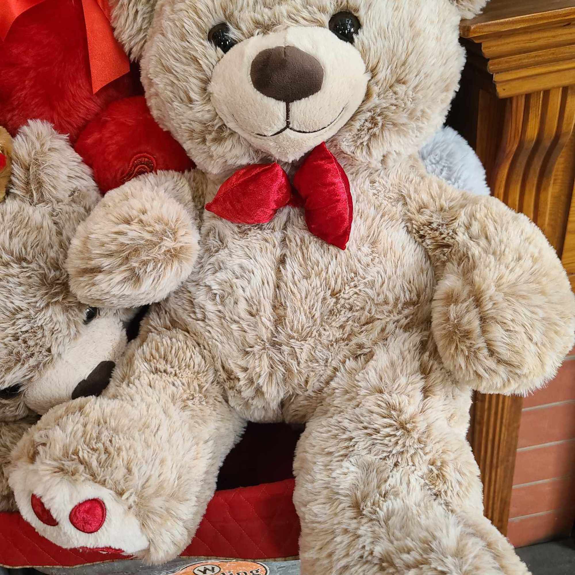 Large plush teddy bear with a red bow sitting among other stuffed bears