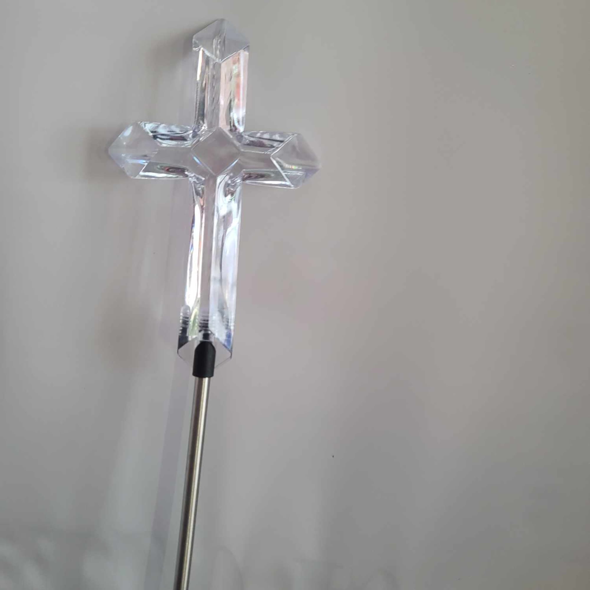Clear crystal cross on a metal stand against a plain background