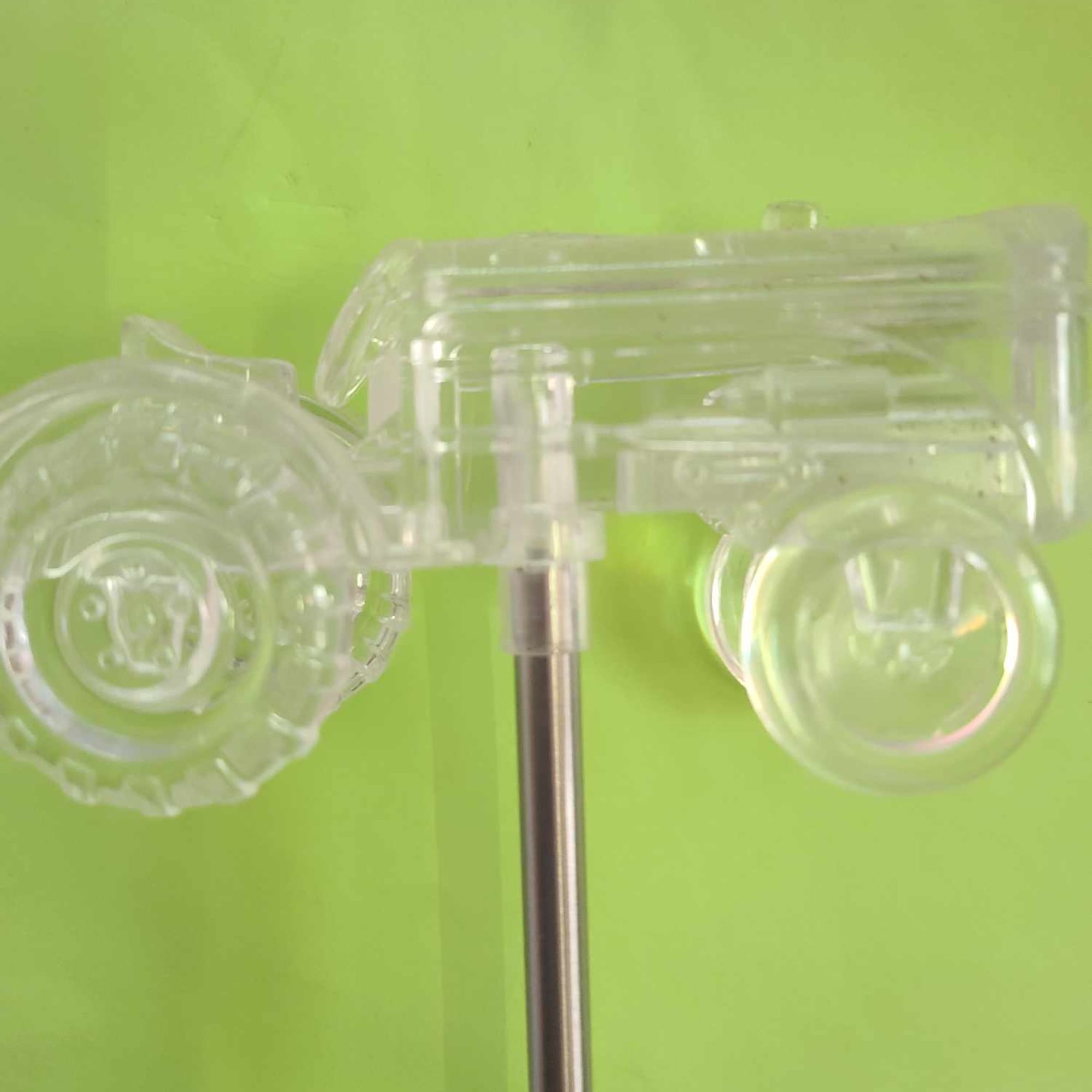 Clear plastic toy car mounted on a metal rod against a green background