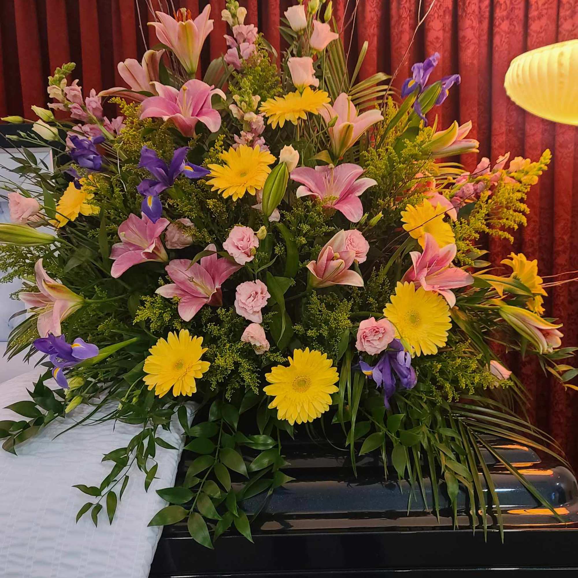 Large floral casket spray with pink lilies, yellow daisies, and purple irises