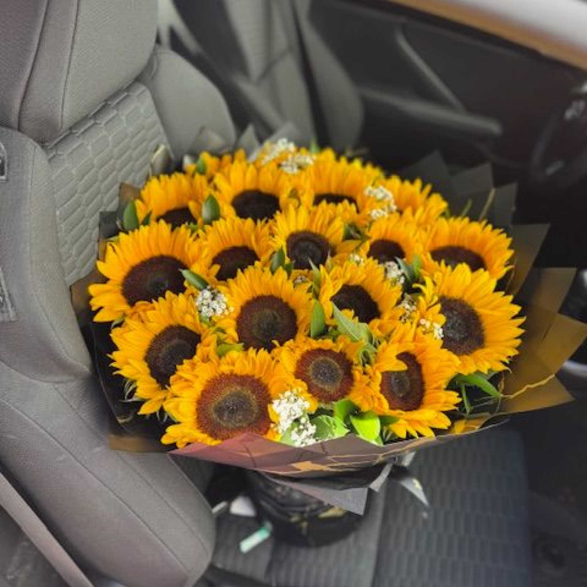 Bouquet of sunflowers wrapped in dark paper on a car seat