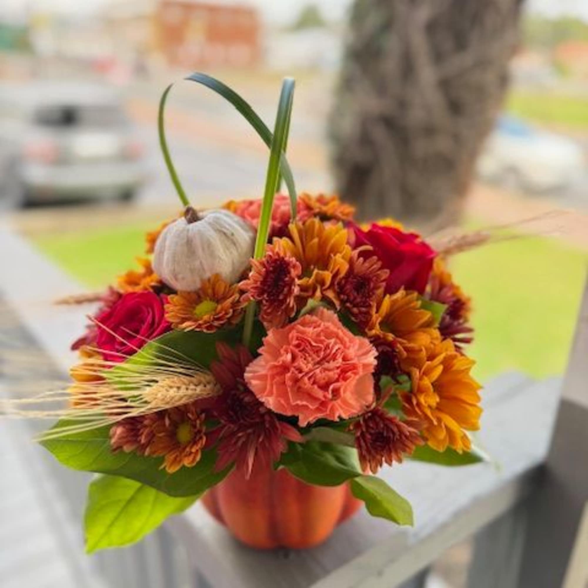 Orange and red mixed flower arrangement in a small pumpkin-shaped container