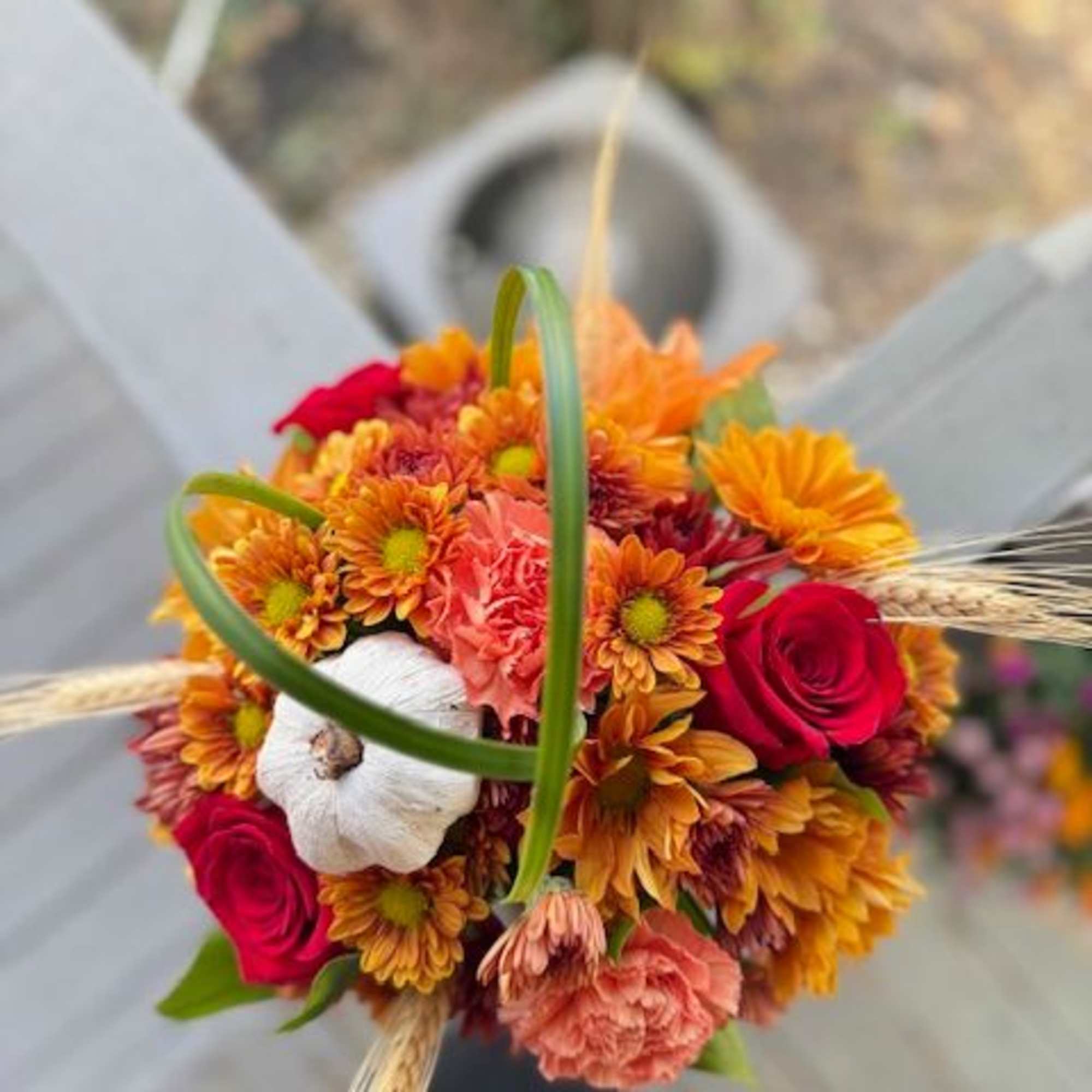 Round bouquet of orange mums, red roses, pink carnations, and a white pumpkin