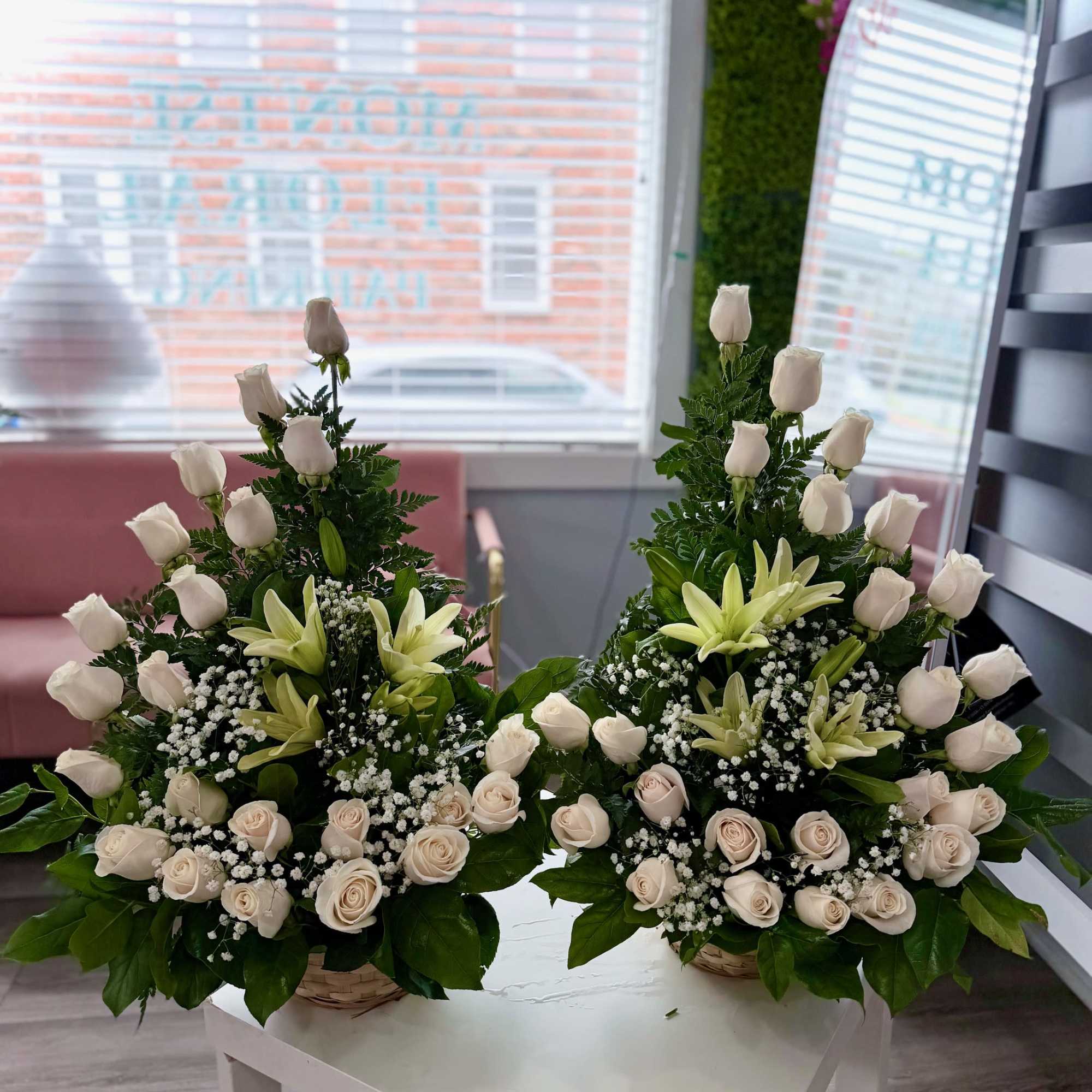 Pair of white rose and lily arrangements in wicker baskets on a white table