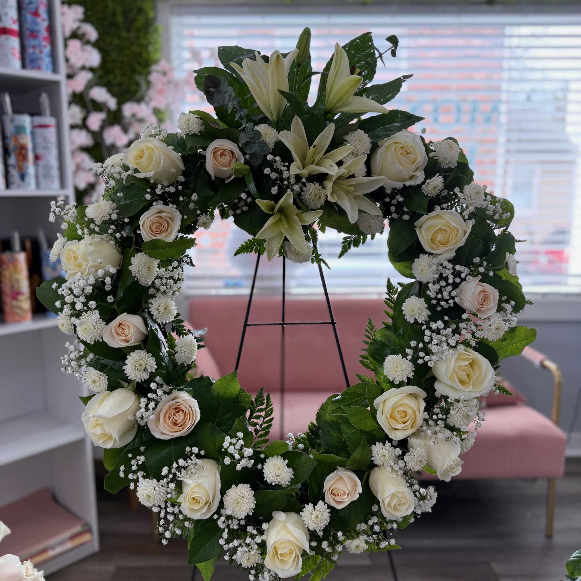 Standing wreath of white lilies, cream roses, and small white blooms on a metal easel