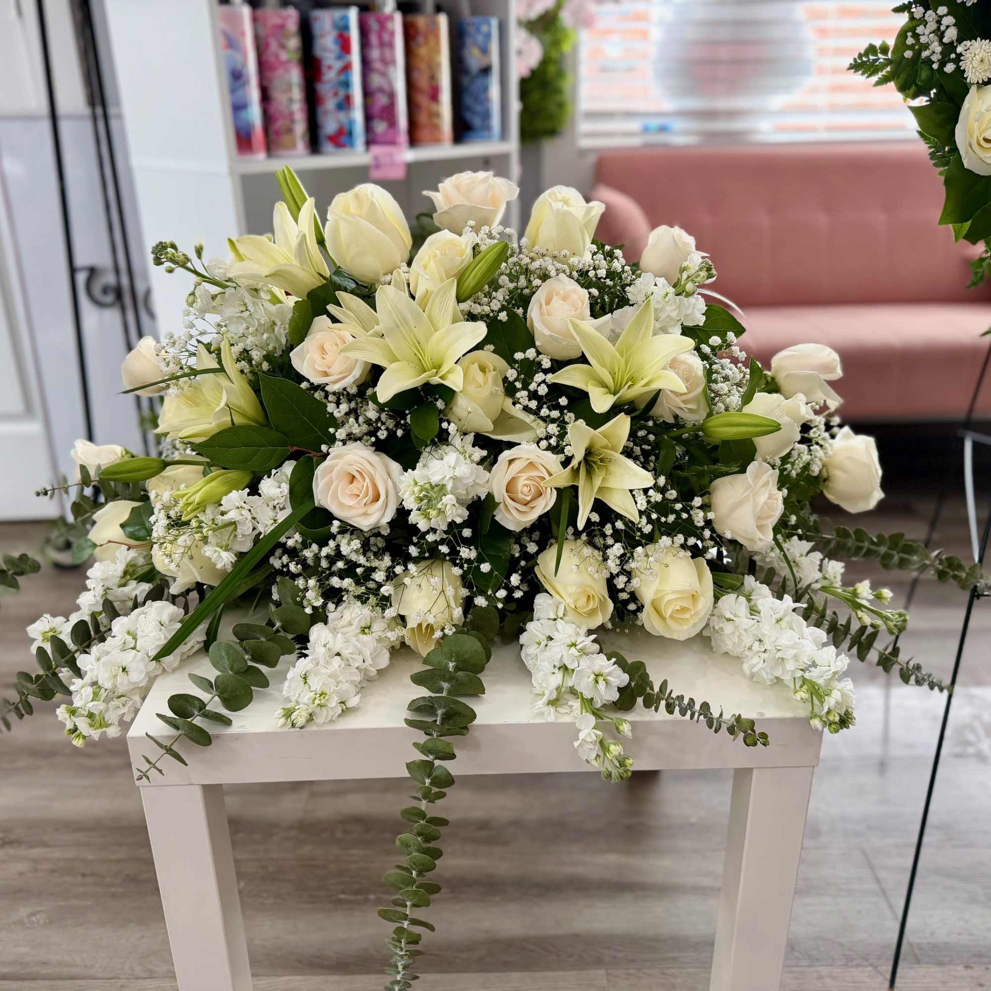 Low white and cream casket-style arrangement with roses and lilies on a white table.
