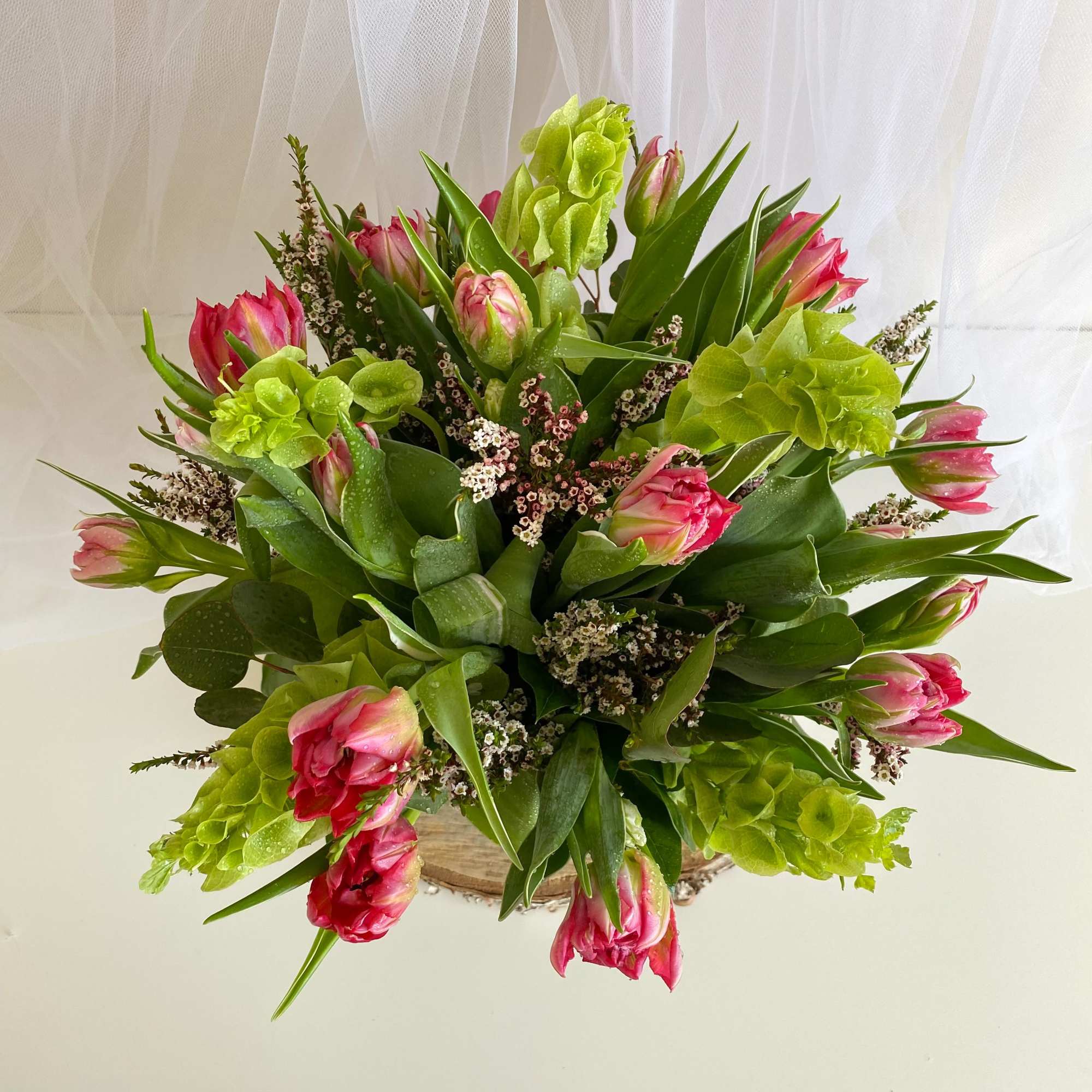 Bouquet of pink tulips and green blooms in a round container