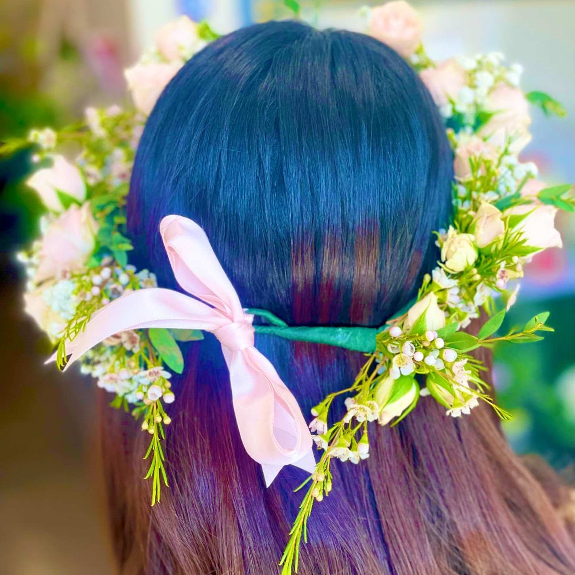Flower crown with pale pink blossoms and a pink ribbon tied around dark hair