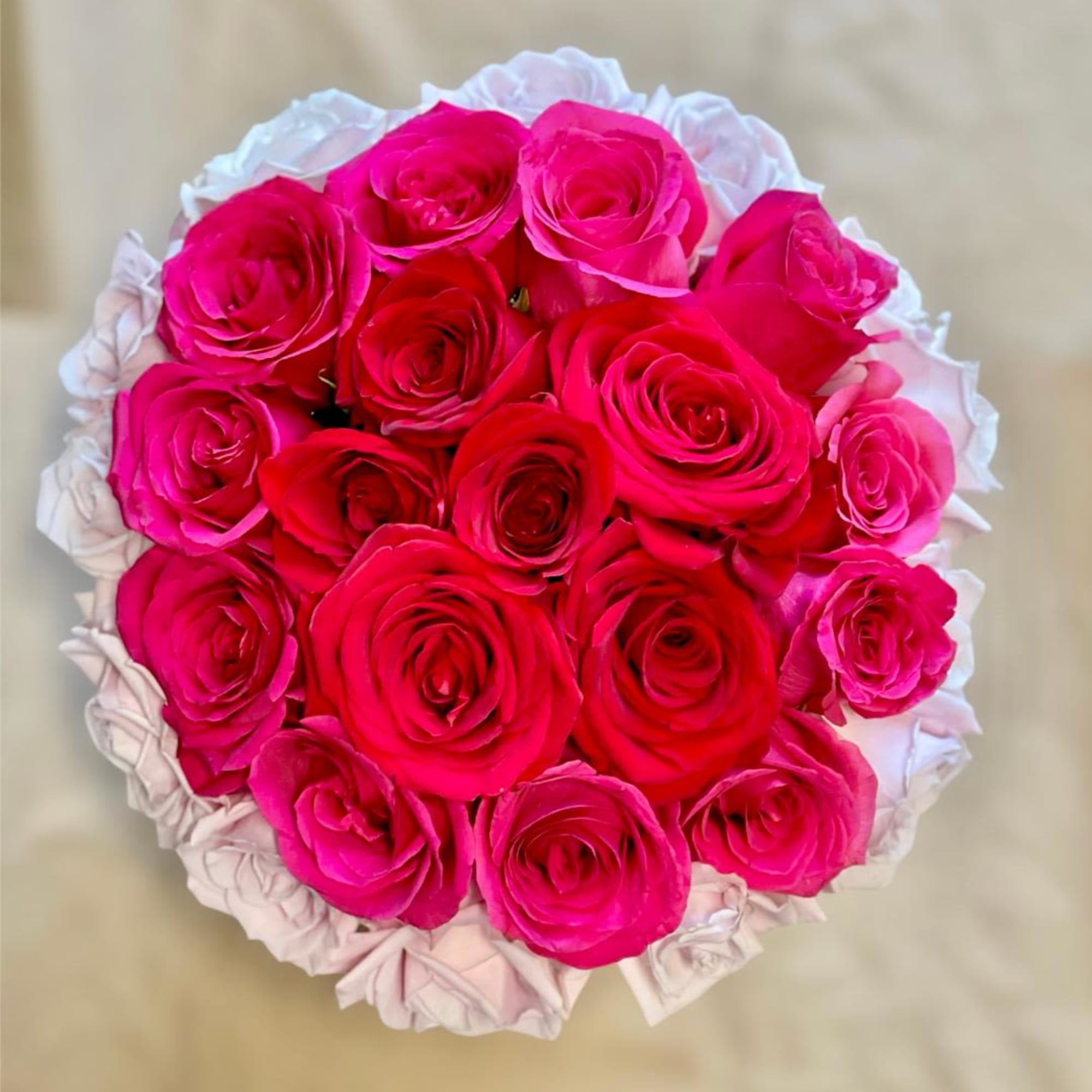 Round bouquet of bright pink and red roses with white wrapping