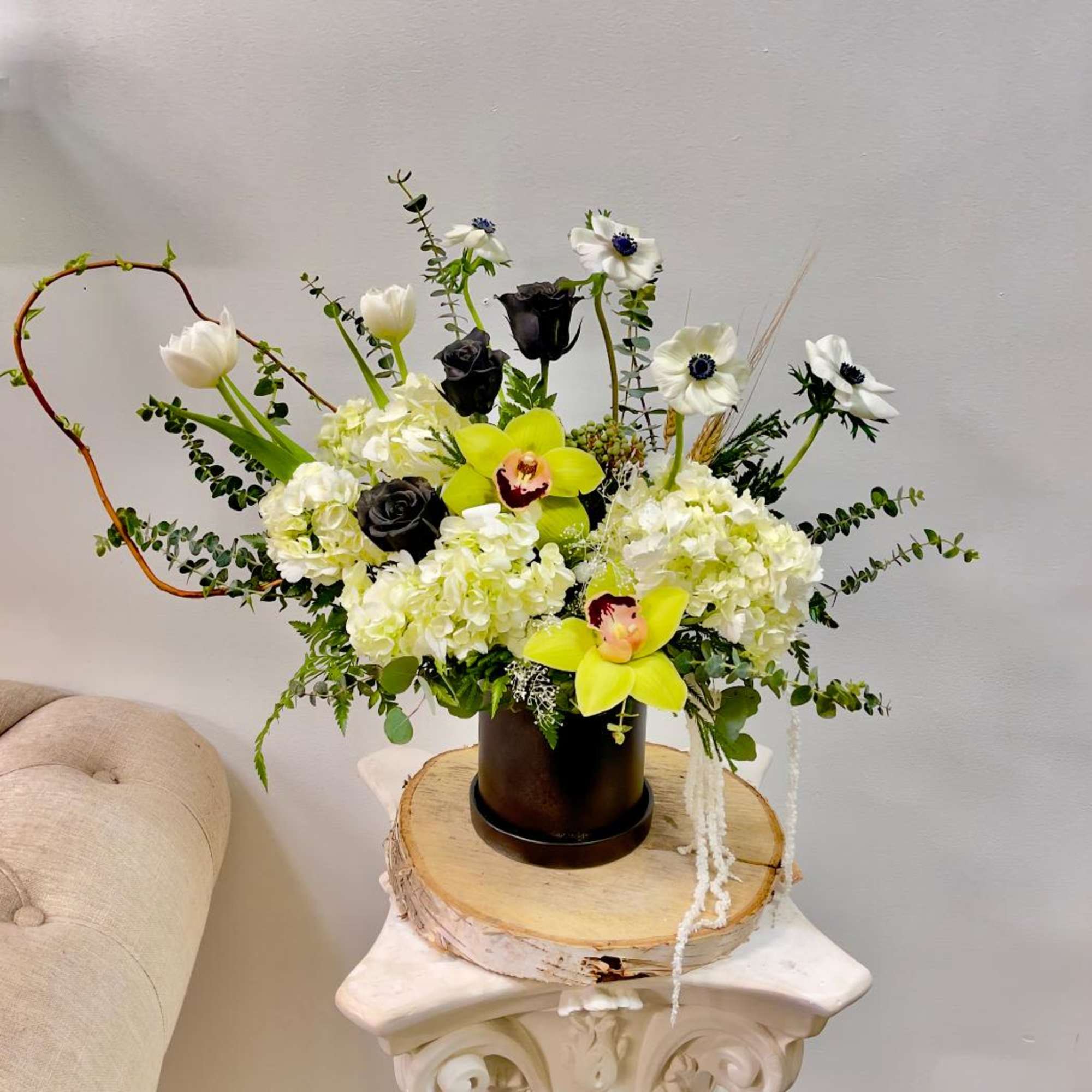 White and black floral arrangement with yellow orchids in a dark vase