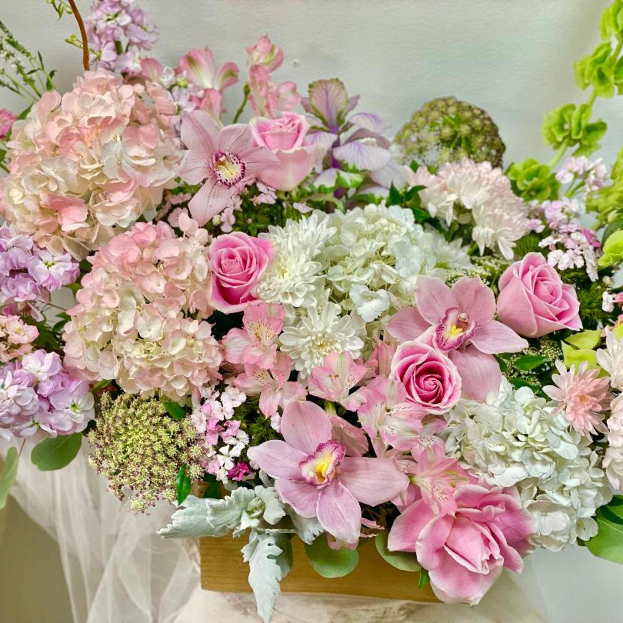 Pink and white floral arrangement with roses, orchids, and hydrangeas in a wooden box