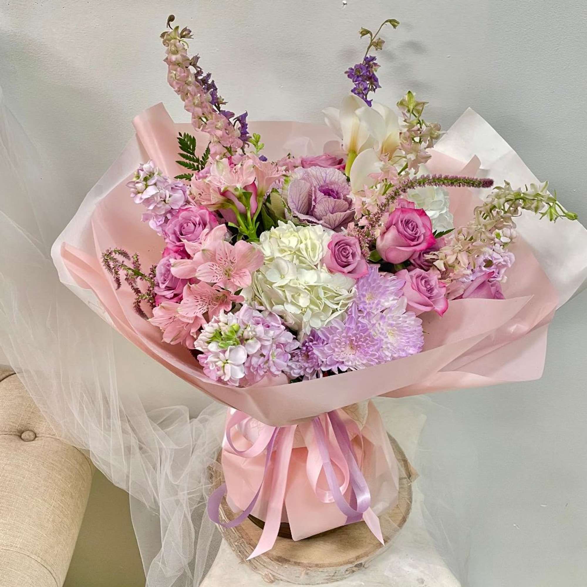 Pink and lavender bouquet with roses, hydrangea, and lilies wrapped in pastel paper