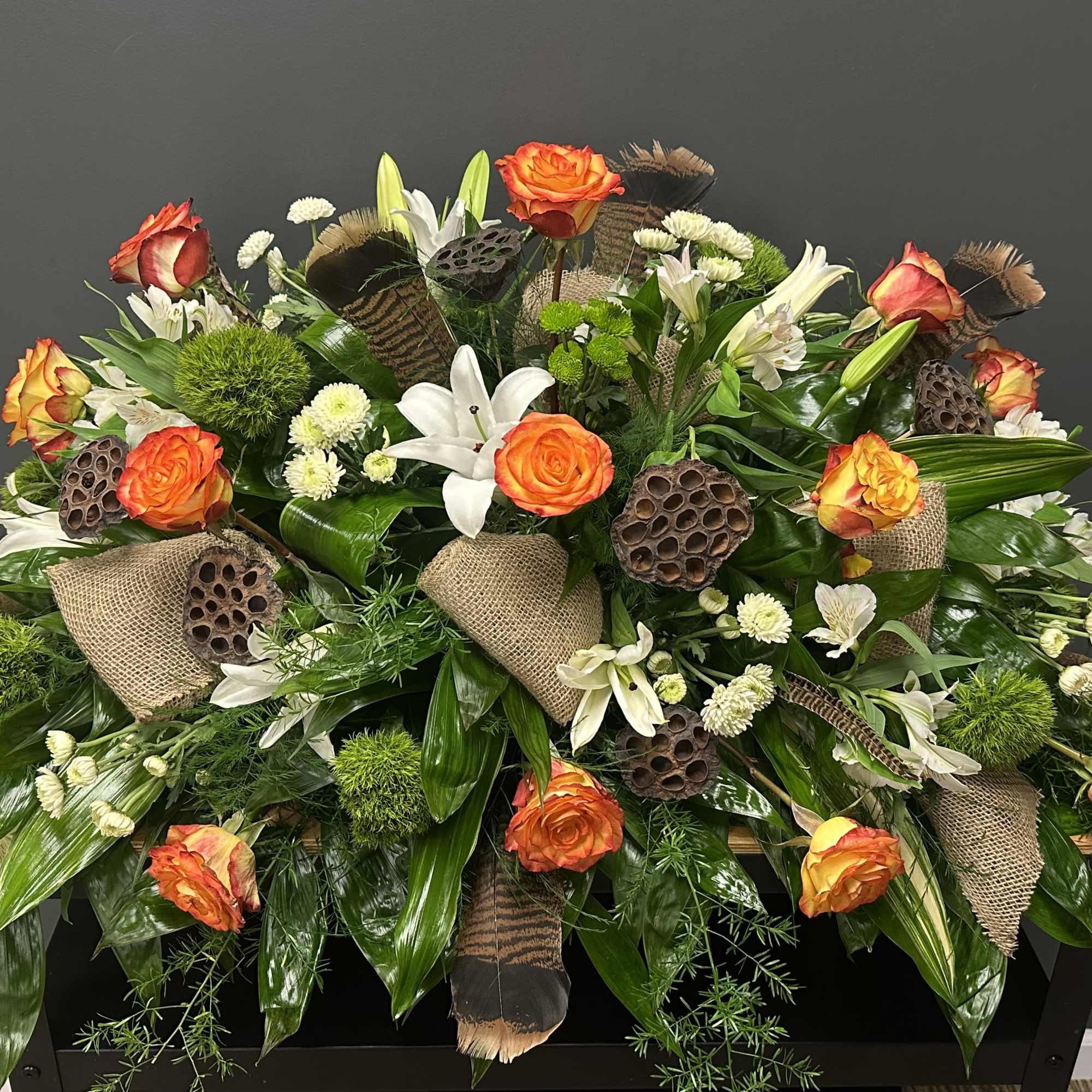 Large floral spray with orange roses, white lilies, and burlap accents