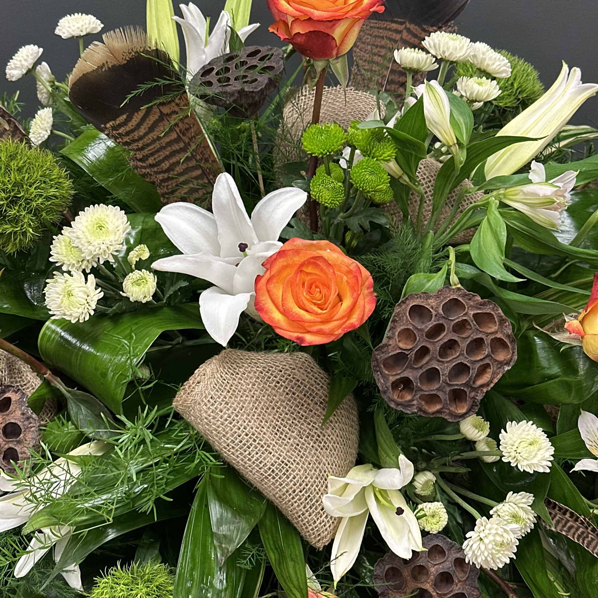Orange roses and white lilies in a lush mixed bouquet with lotus pods