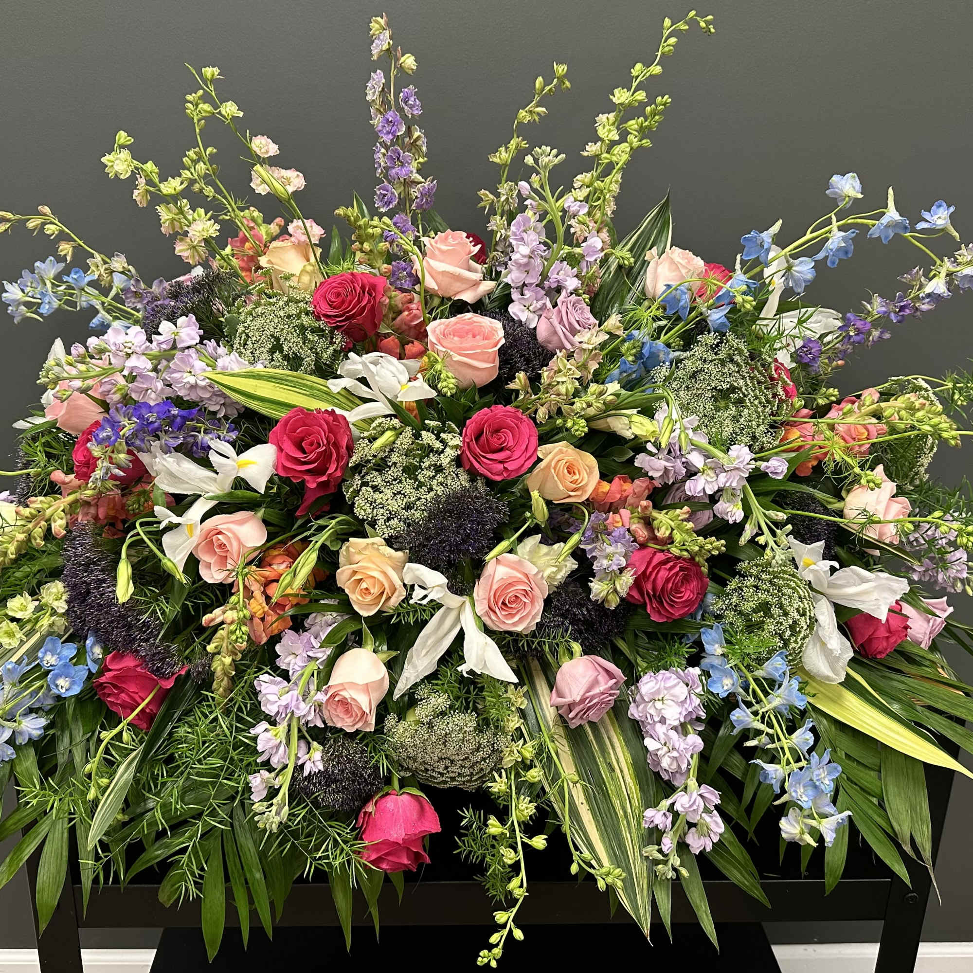 Large mixed floral arrangement with roses, lilies, and blue delphinium