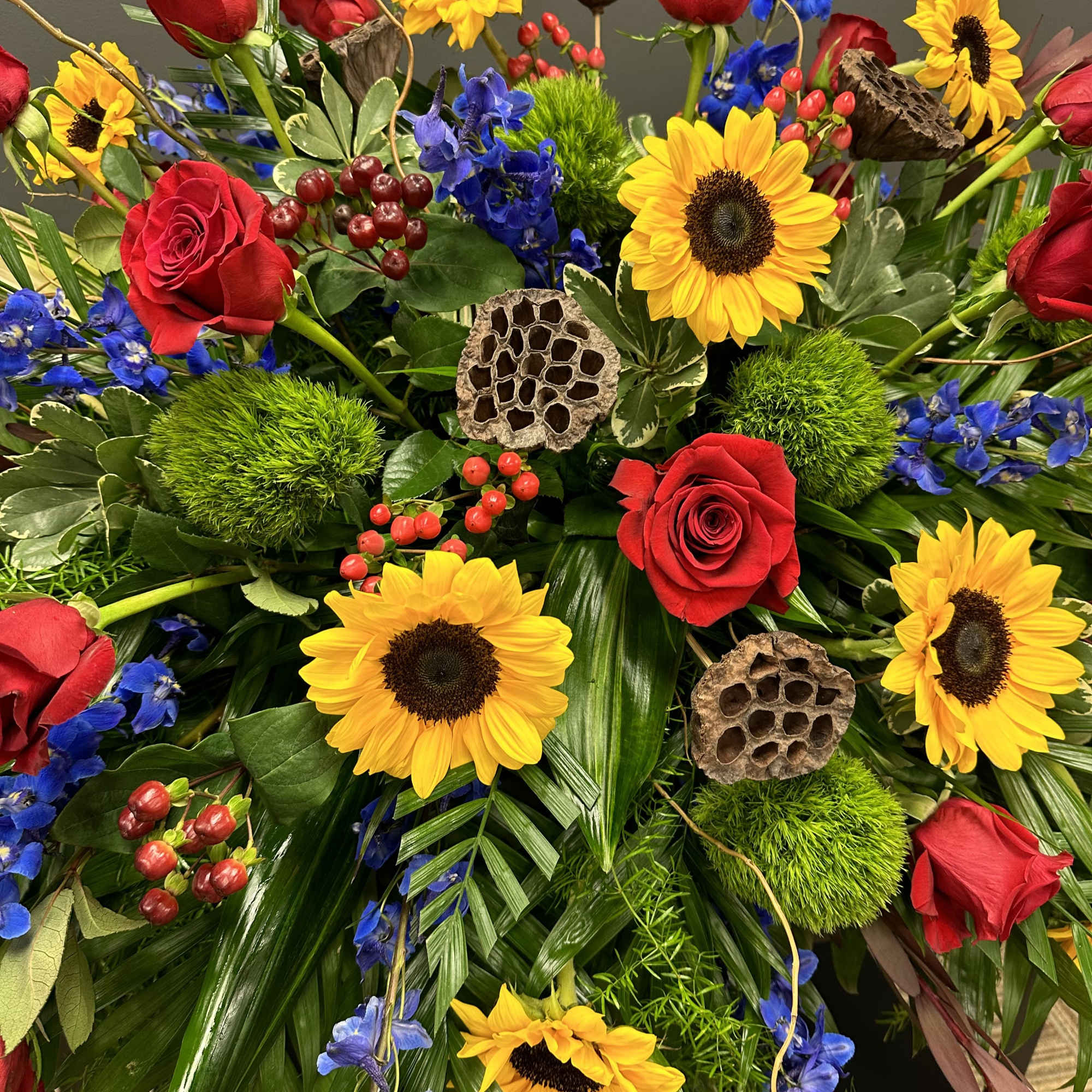 Bouquet of red roses, sunflowers, and blue flowers with decorative pods