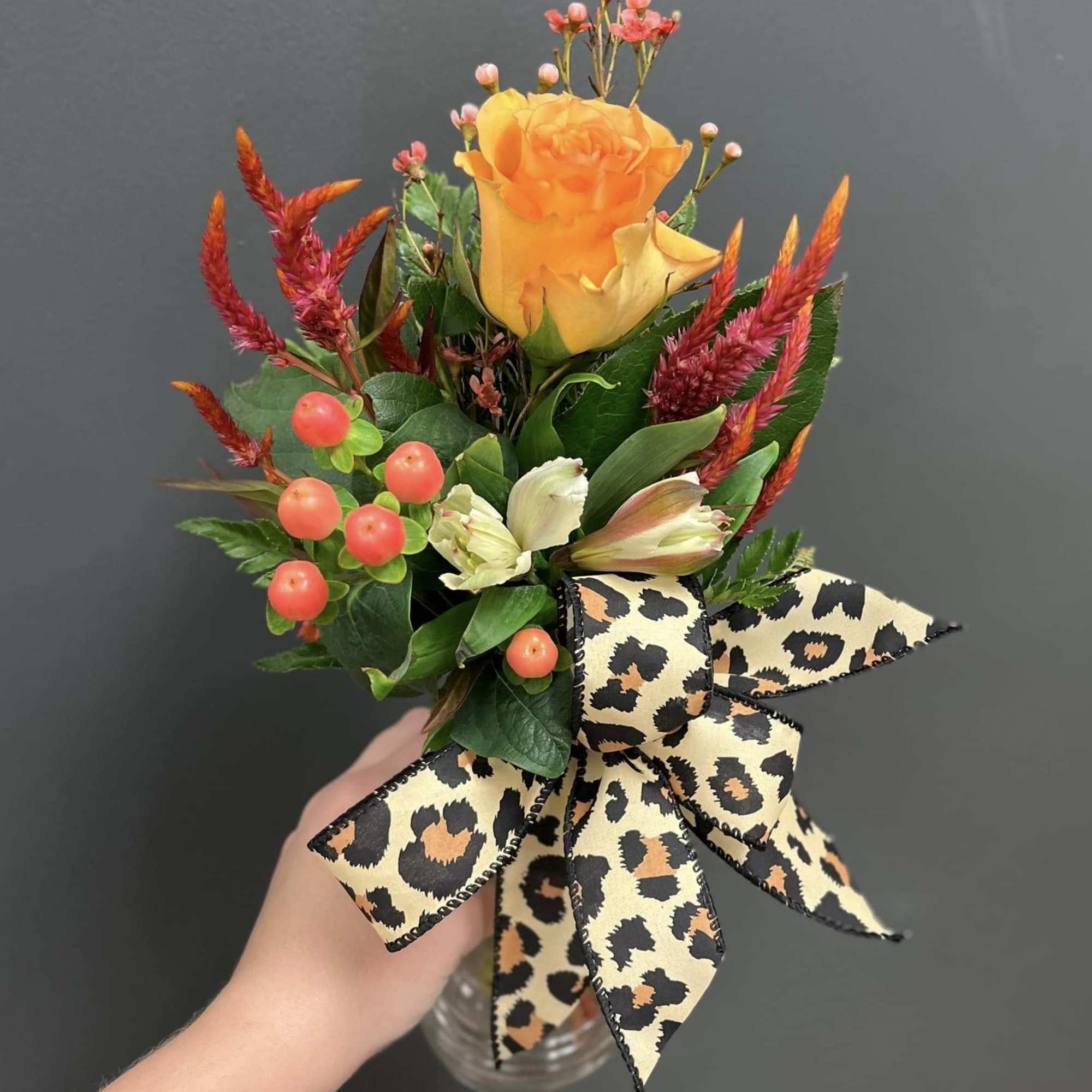 Small bouquet with an orange rose, berries, and a leopard-print bow in a glass vase