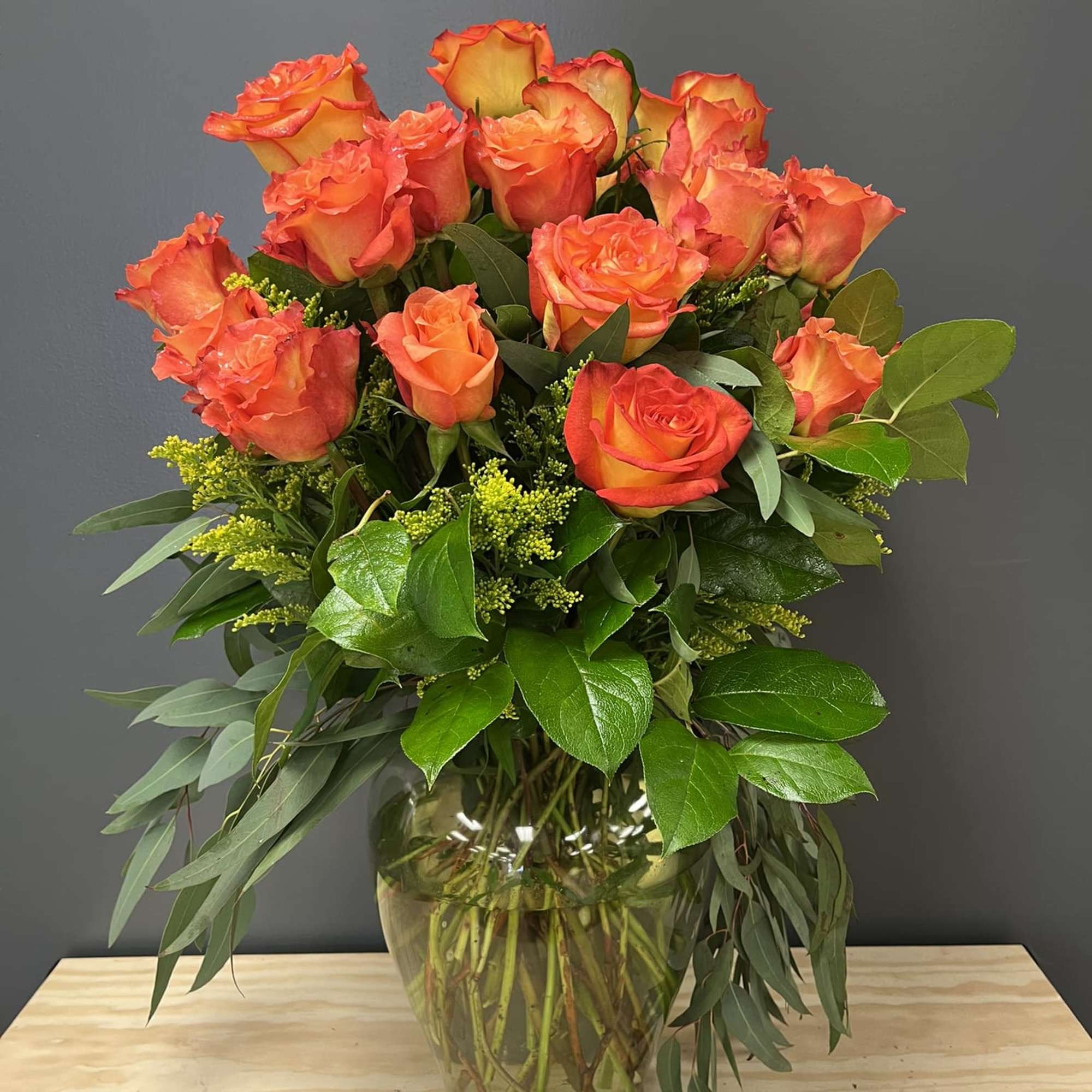 Orange roses arranged in a glass vase with greenery