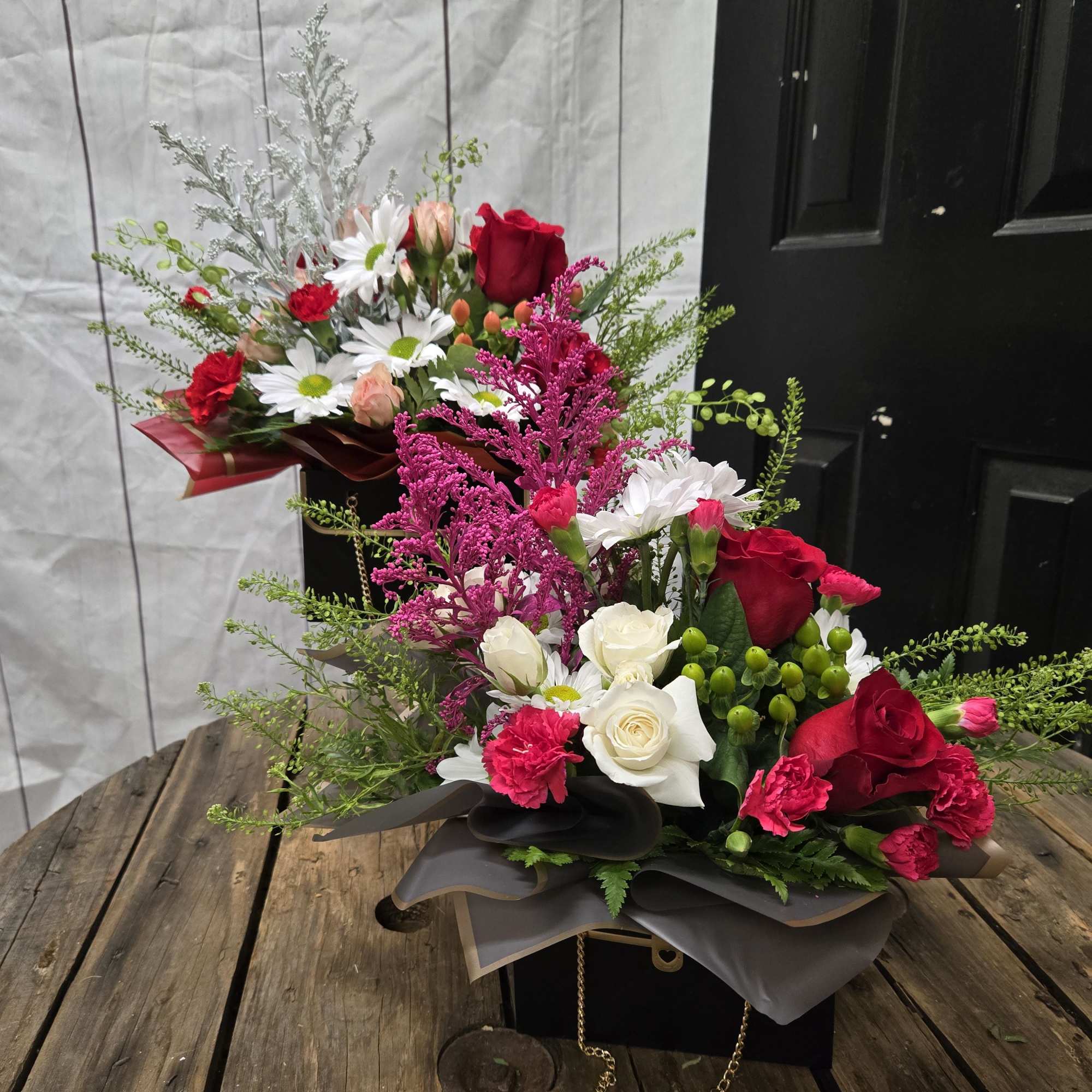Two floral arrangements in black boxes with red, white, and pink blooms