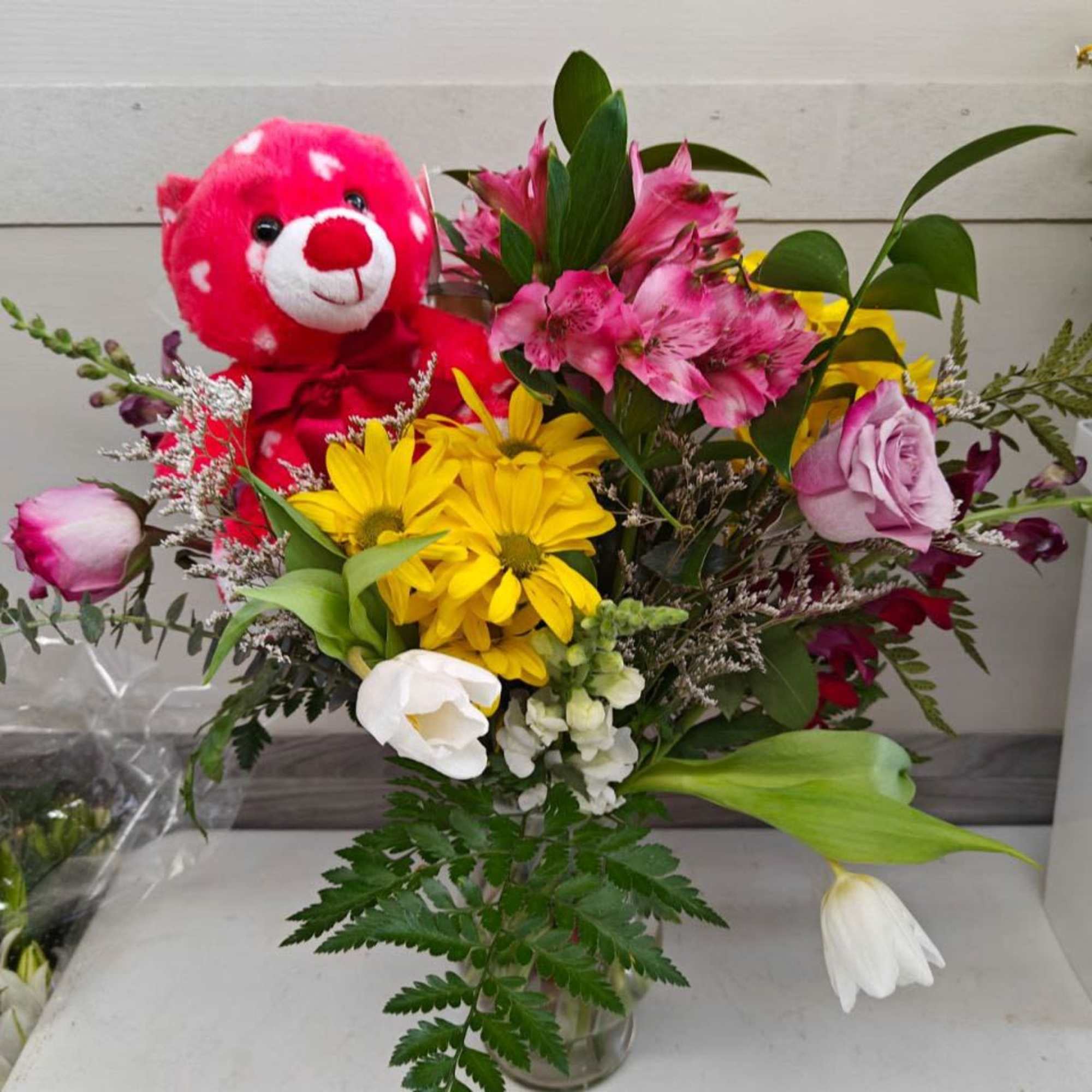 Bouquet of mixed flowers with a pink teddy bear in a glass vase