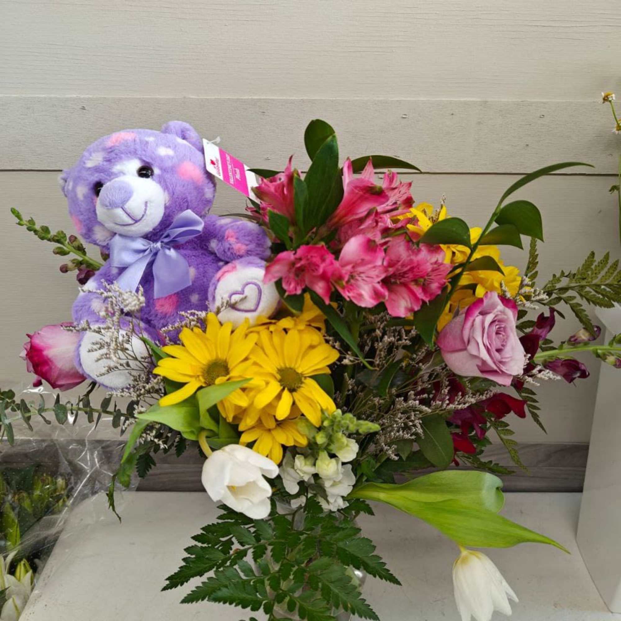 Mixed flower bouquet with a purple teddy bear and bright blooms in a vase