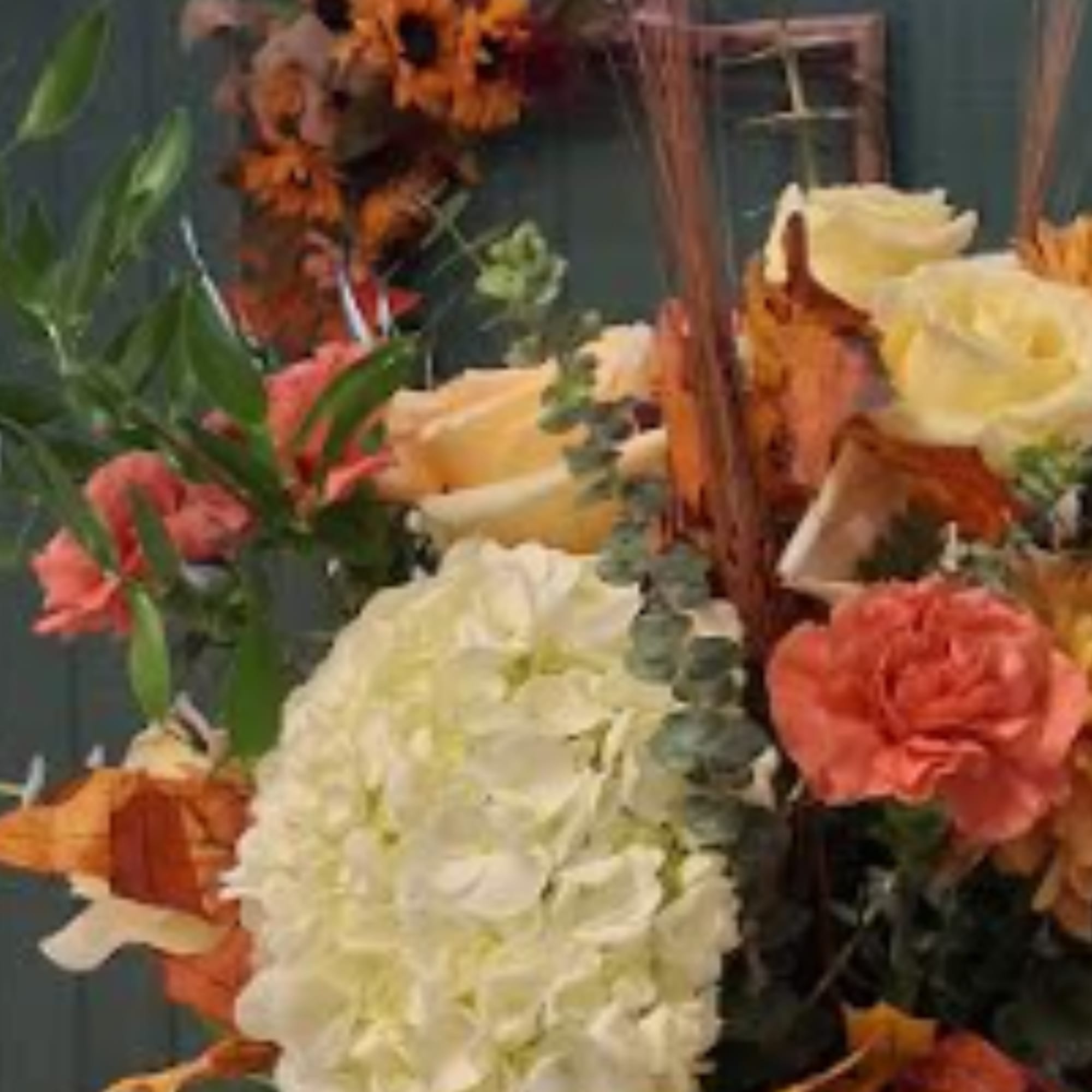 Arrangement of white hydrangea, cream roses, and orange flowers in a basket