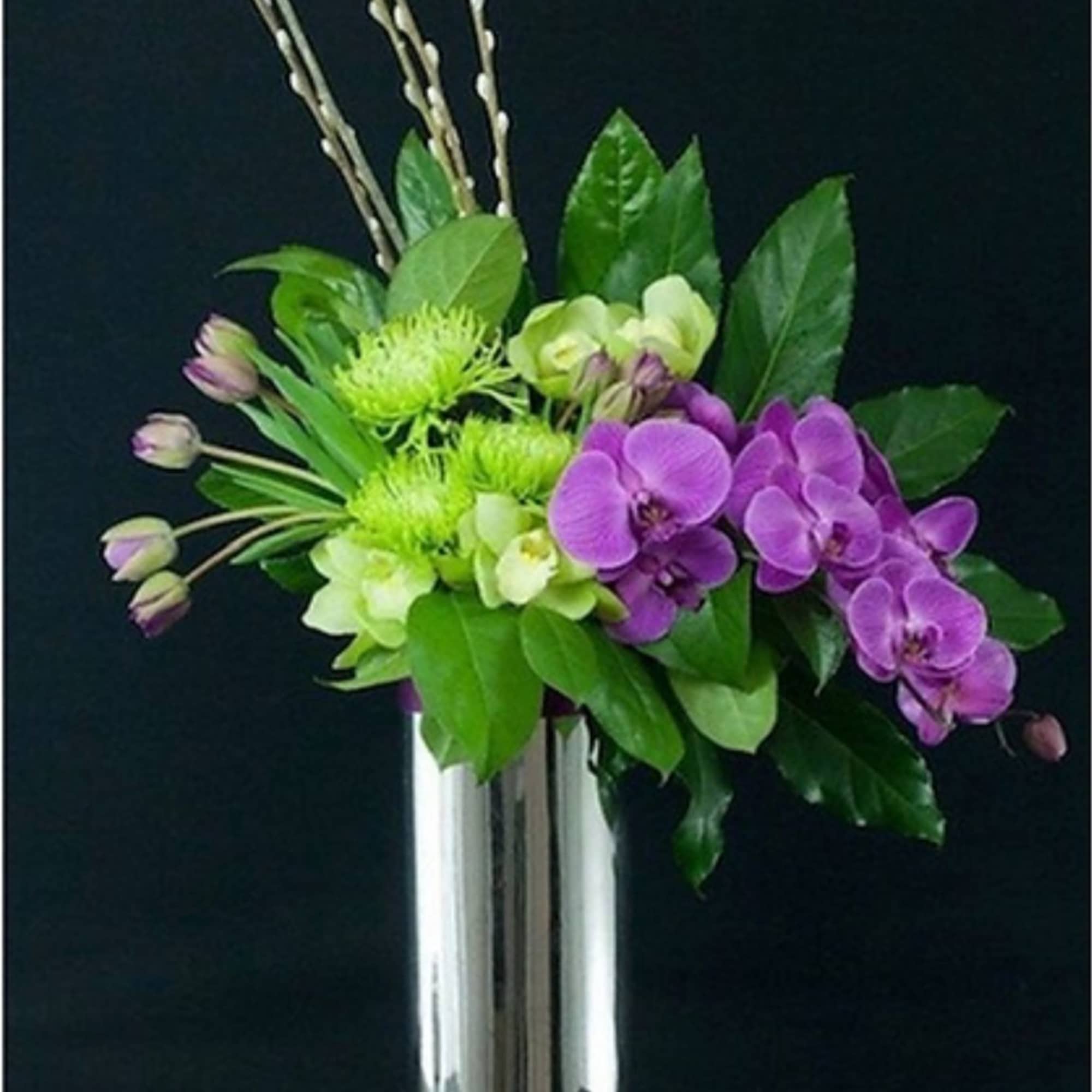 Purple orchids and green blooms in a tall silver vase