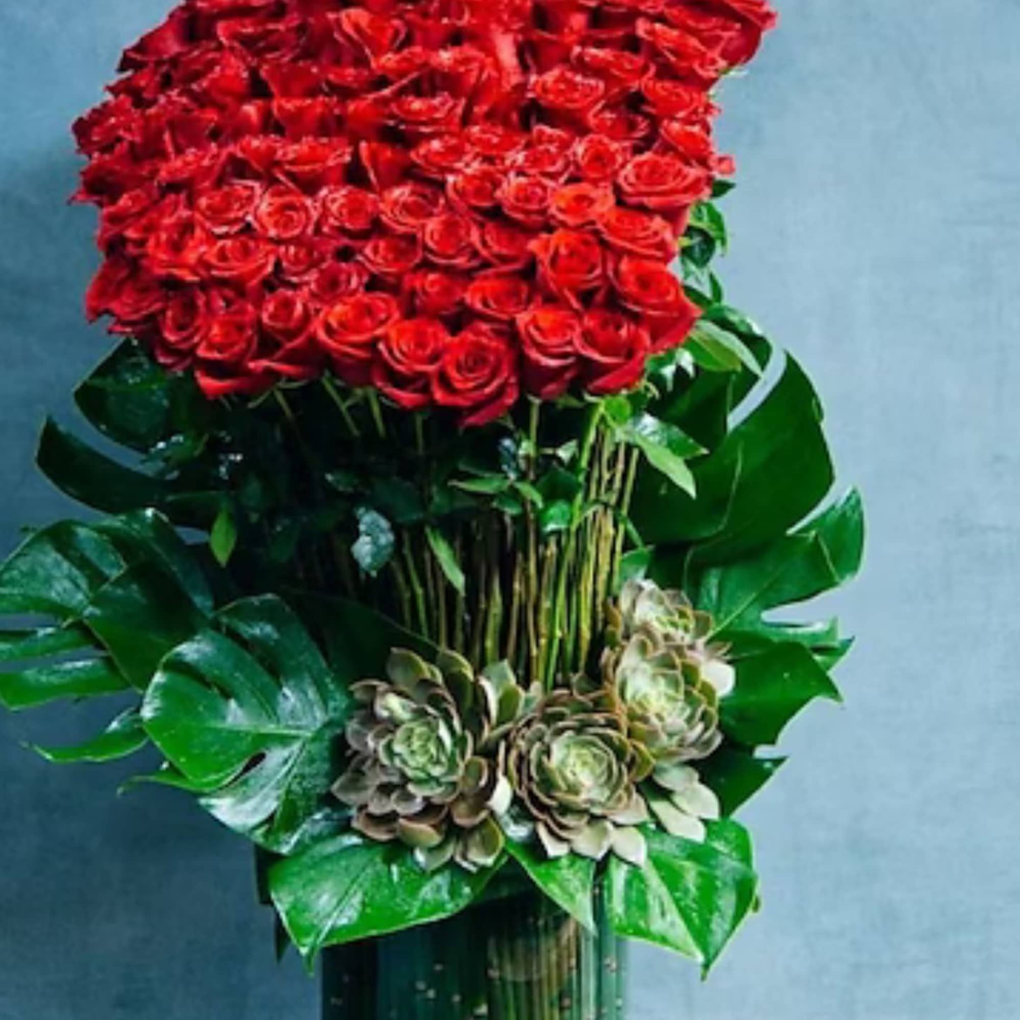 Large red rose arrangement in a tall green vase with succulents