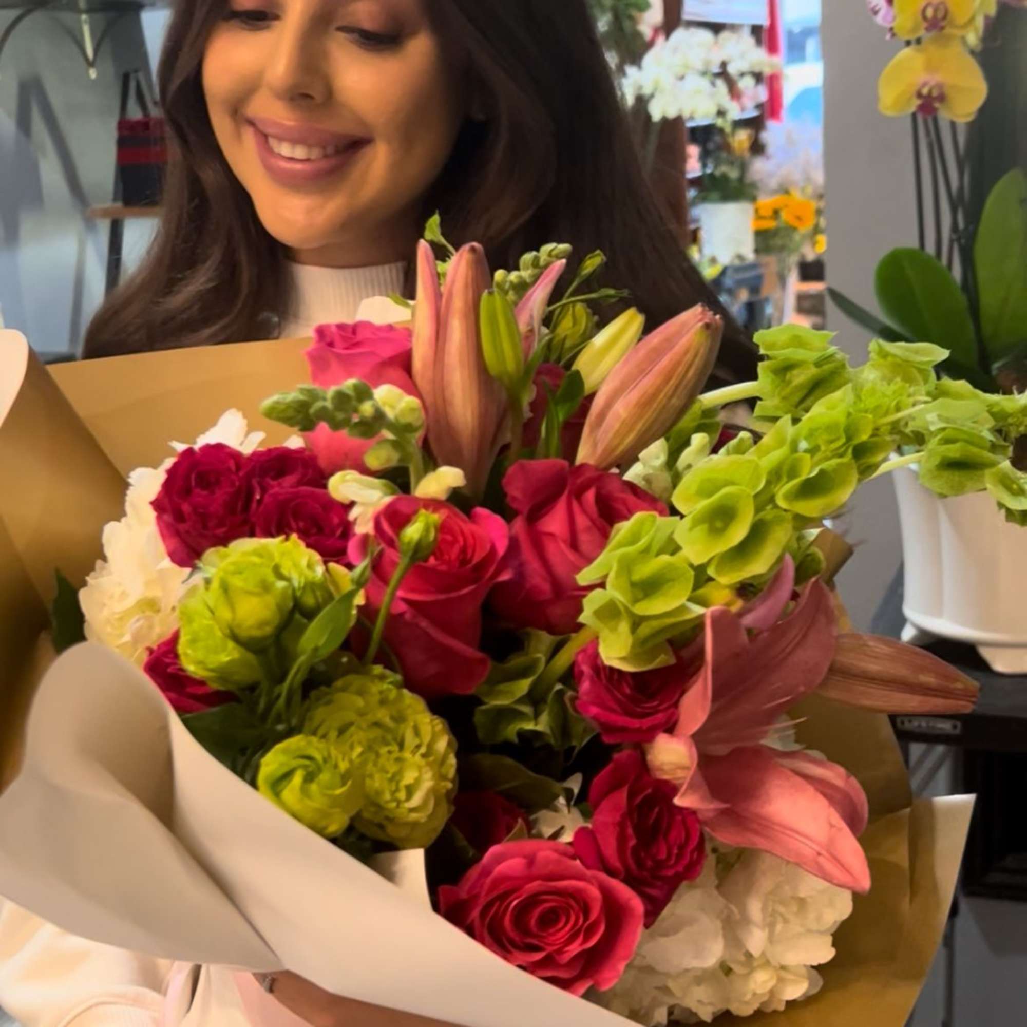 Woman holding a colorful bouquet of roses, lilies, and green blooms