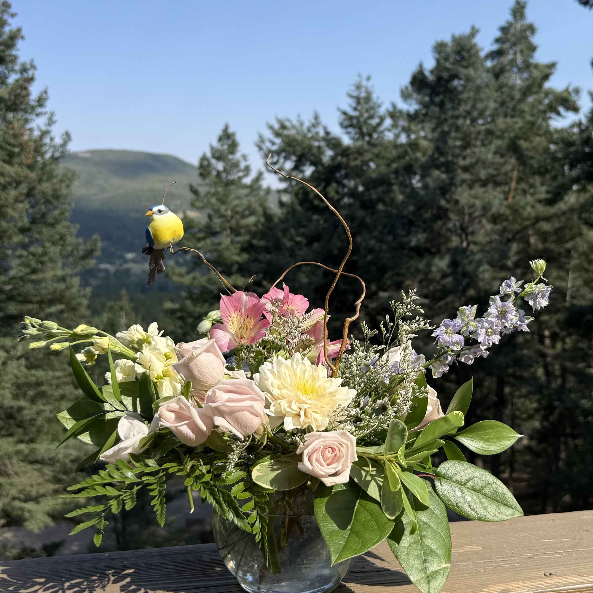 Mixed pastel bouquet in a clear glass vase with a bird ornament